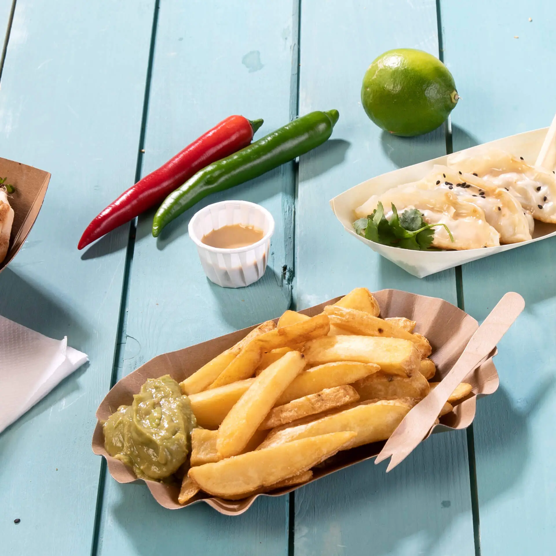 Plate of golden fries served with green sauce and nearby condiments, including red and green chilies, a lime, and dumplings.