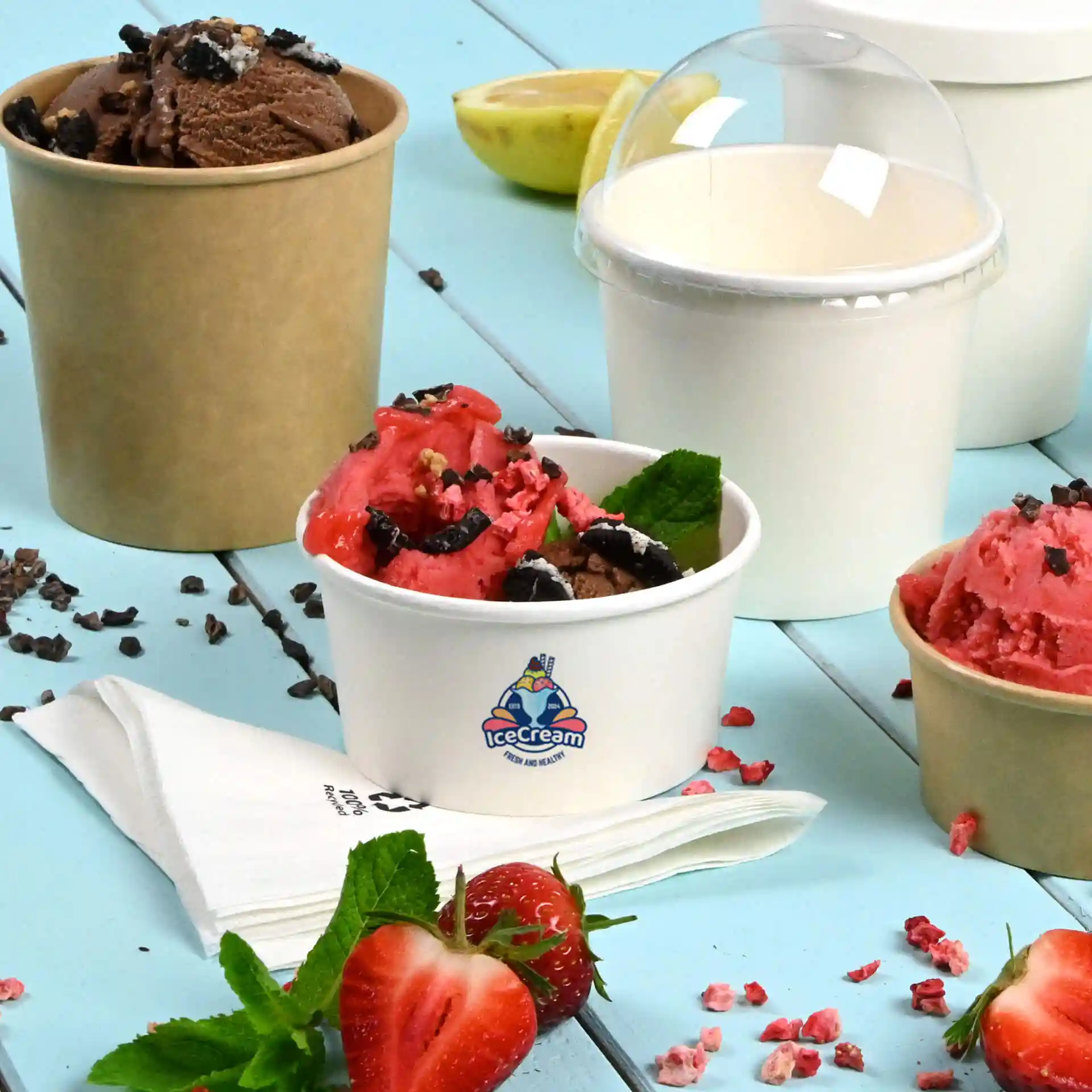 Bild von mehreren Eiskugeln: ein weißer Becher mit Logo, gefüllt mit pinkem und braunem Eis, ein brauner Becher mit Schokoladeneis und ein schlichter weißer Becher.