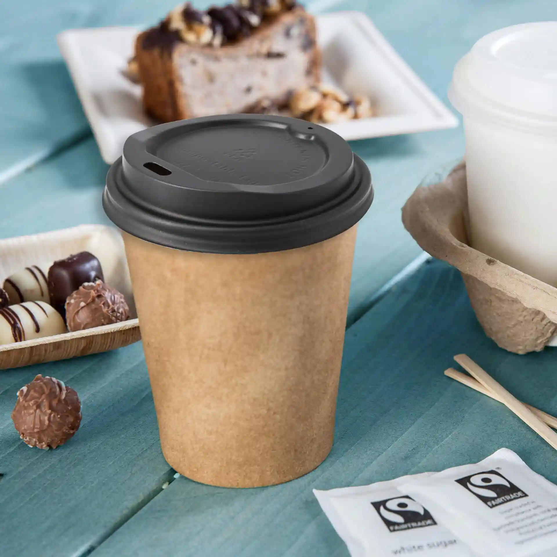 Black CPLA coffee cup lid with a drinking hole, placed on a blue wooden surface with snacks nearby.