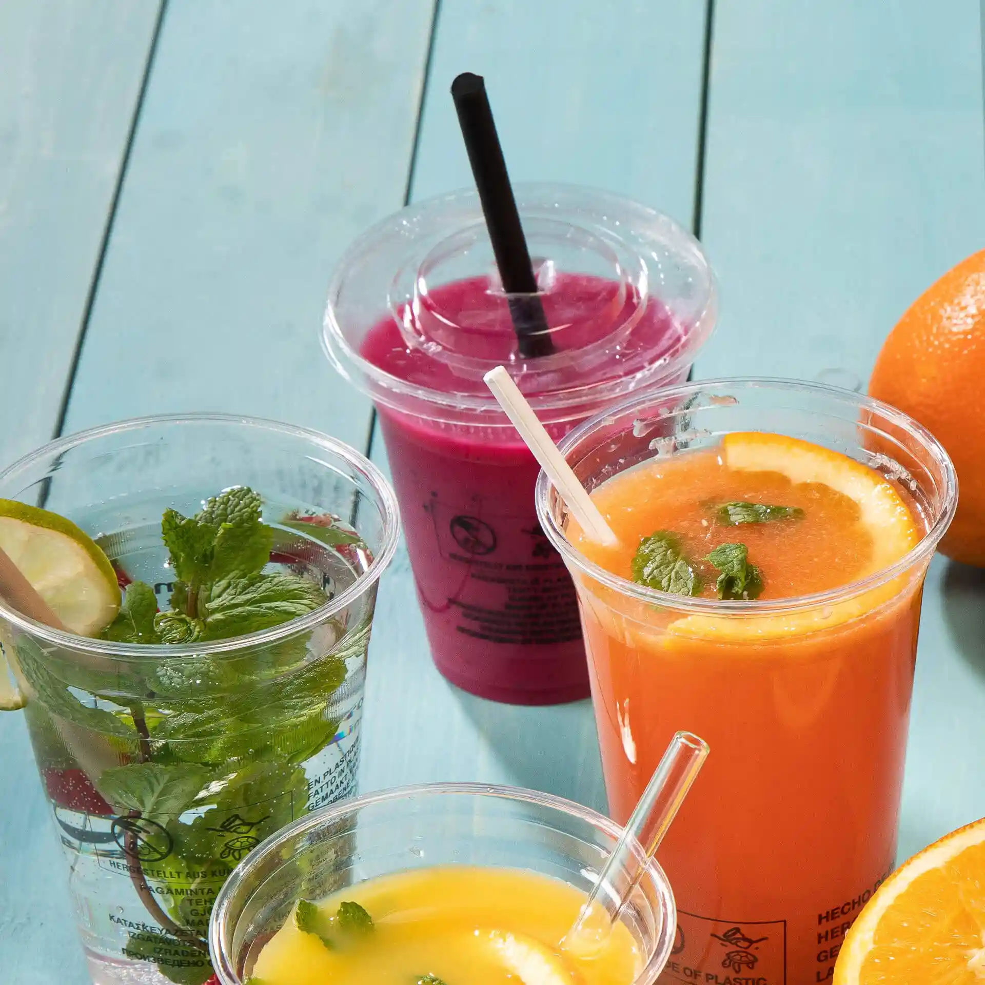 Image of several clear cups with drinks: mint water, orange juice with mint, and a pink beverage, on a blue surface.