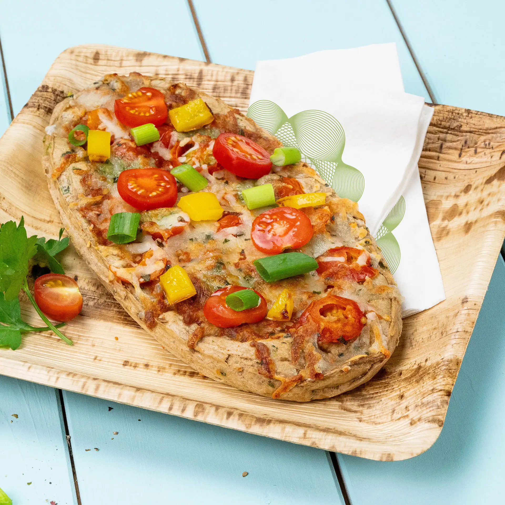Vegetarian pizza topped with cherry tomatoes, bell peppers, and green onions on a wooden plate with a napkin.