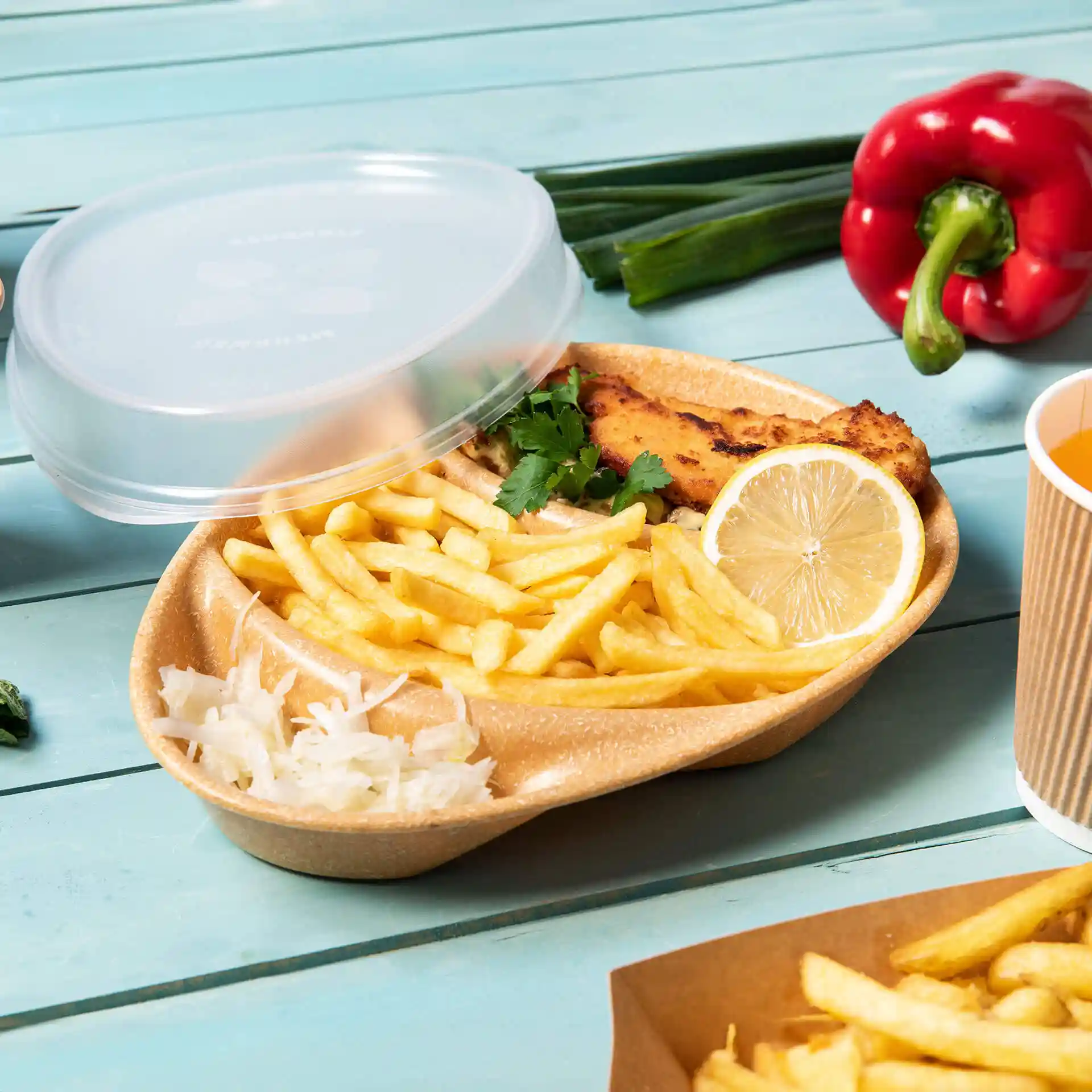 Brown reusable plate with three compartments, containing fries, fish, lemon, and cilantro, with a clear lid on top.