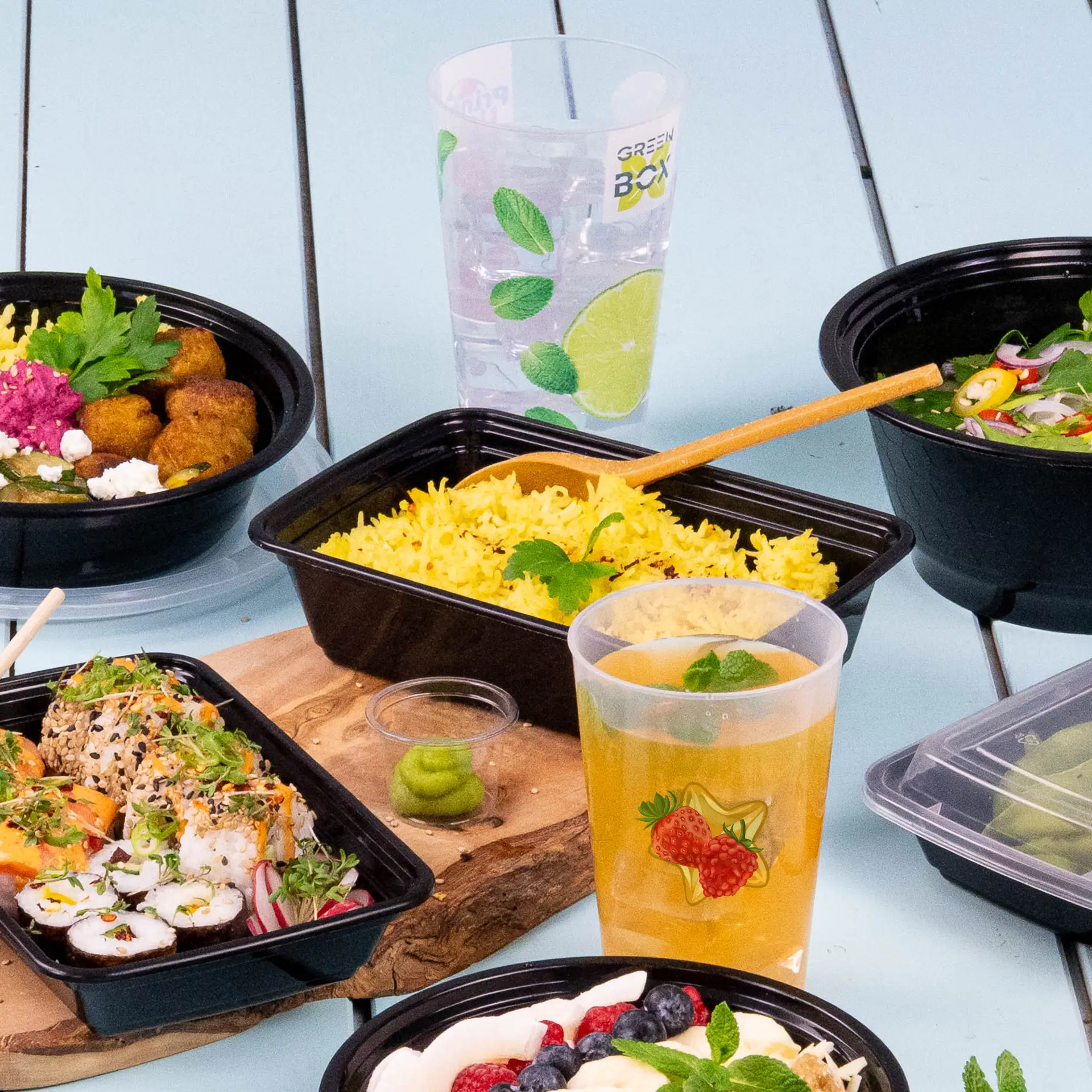 A reusable cup with a printed logo, alongside assorted food containers containing rice, sushi, and beverages.