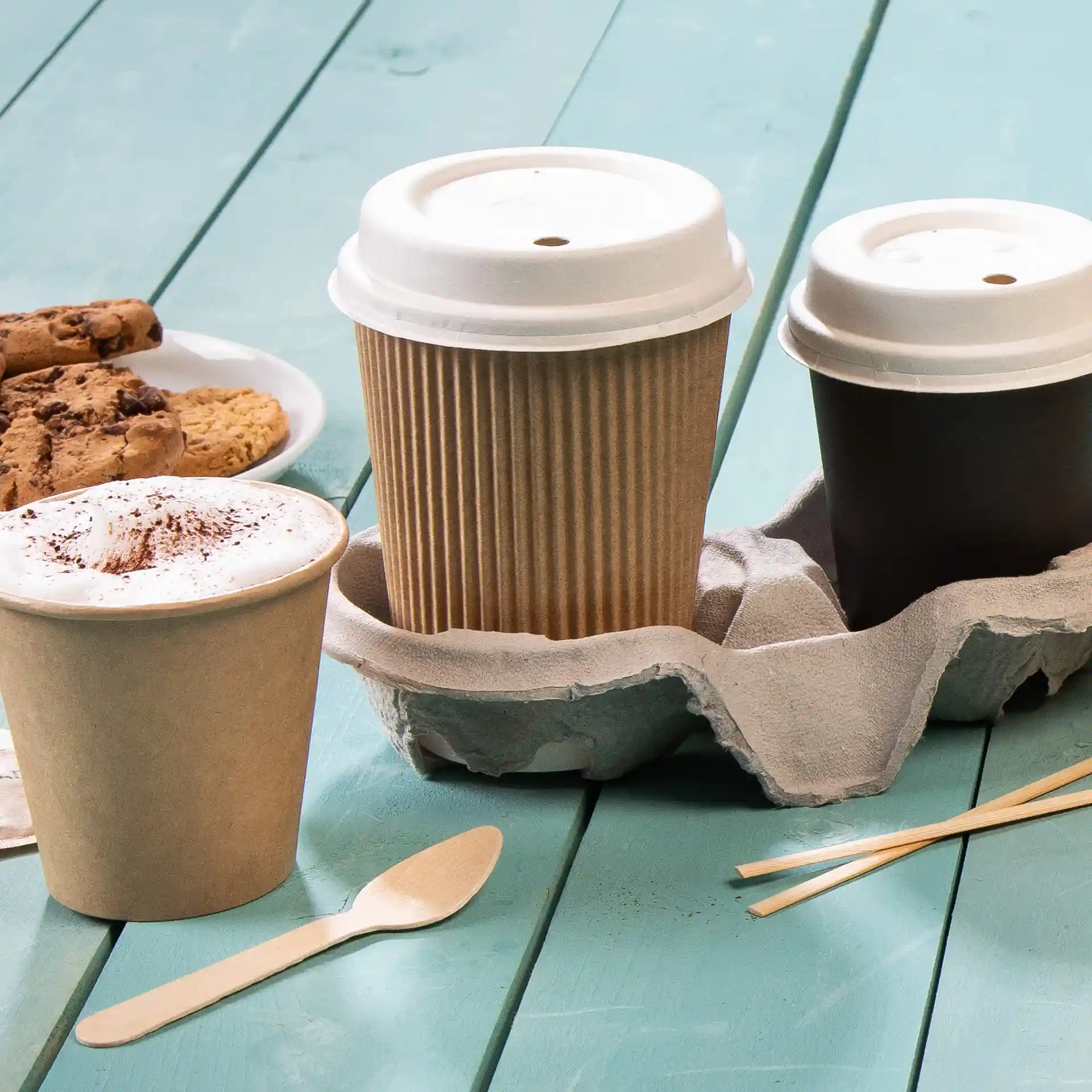 Image of a take-away coffee cup in a cardboard holder, with a brown ripple cup and a plain brown cup, alongside a spoon and cookies.