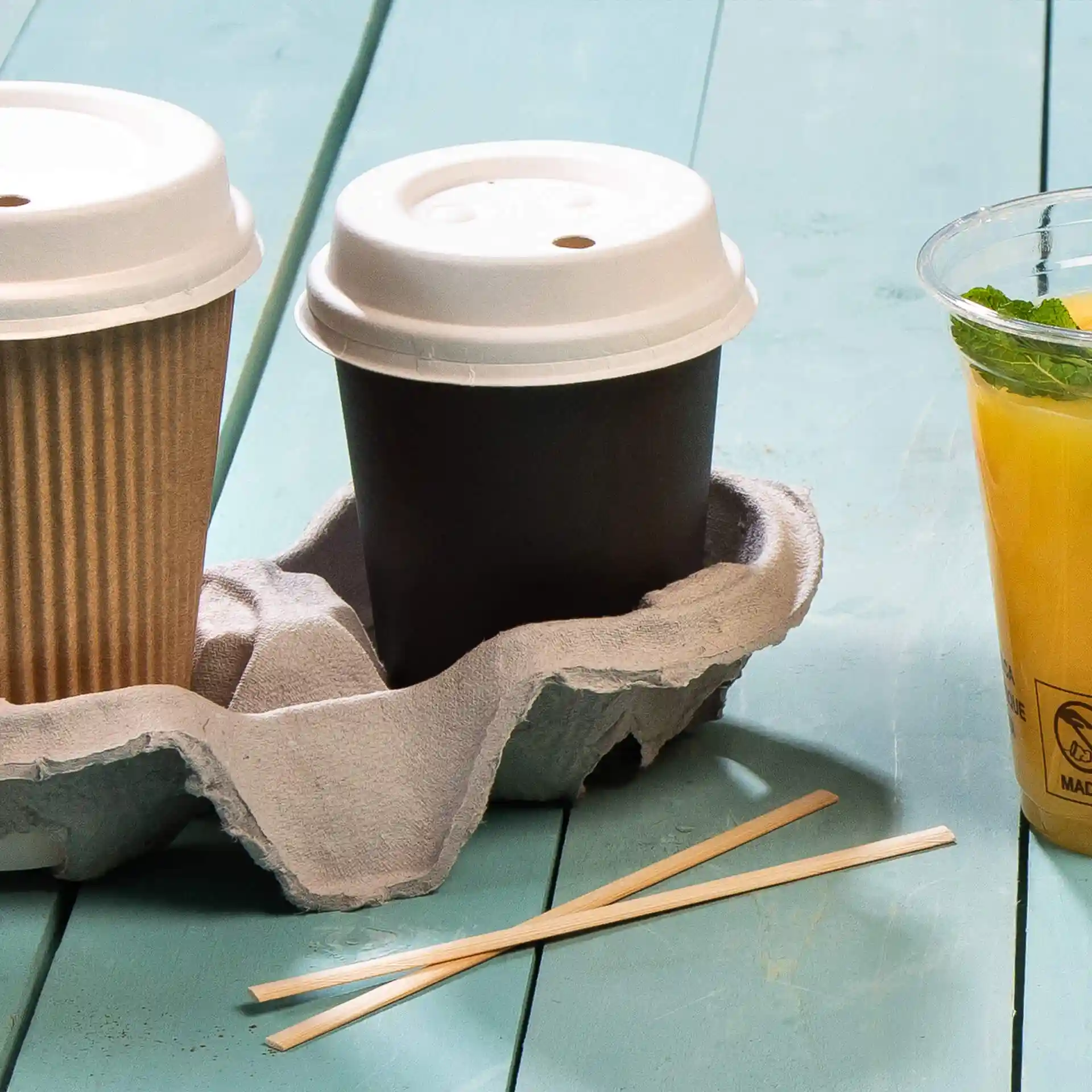 Image of two coffee cups in a gray cardboard holder, with bamboo stirrers beside them on a blue surface.