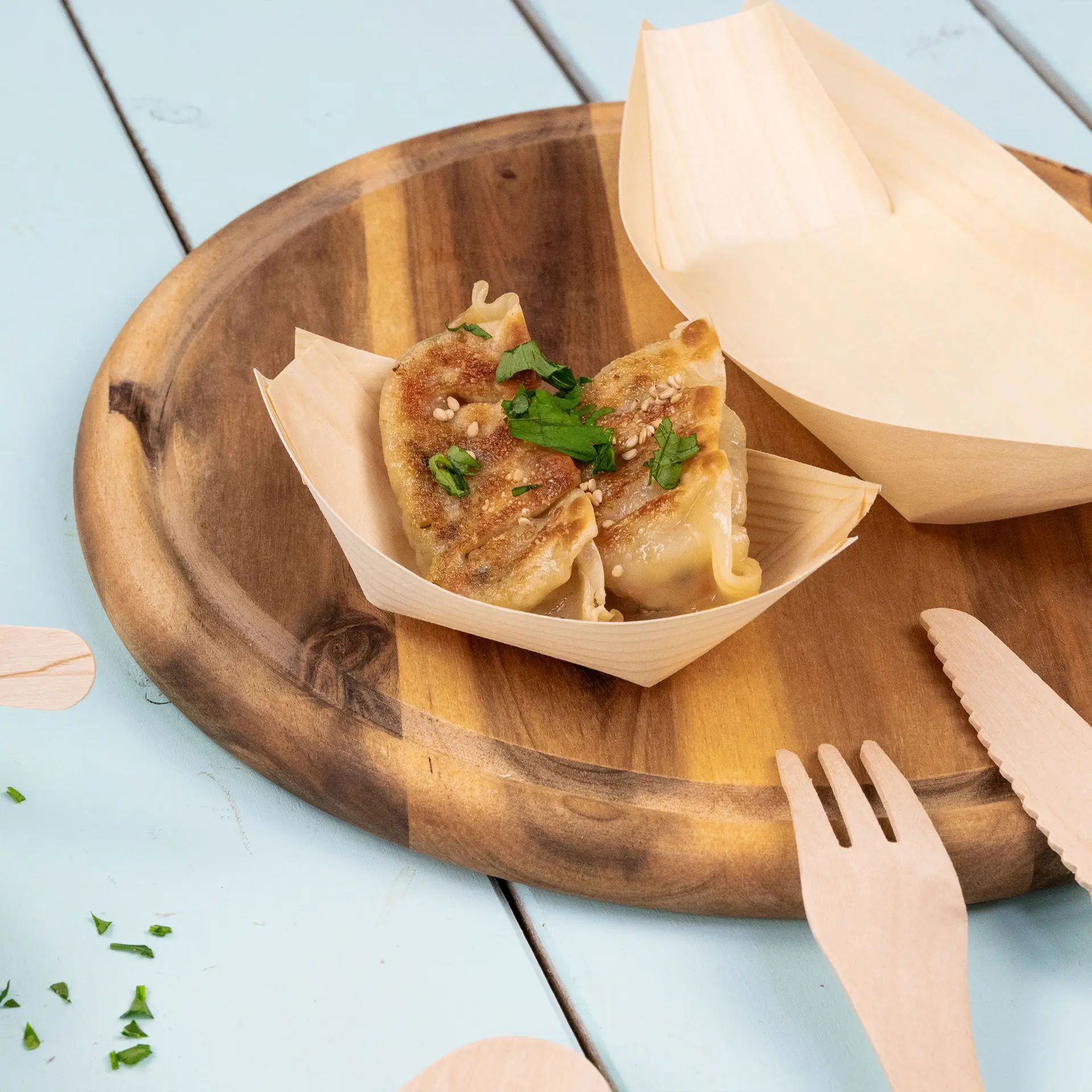 Wooden boat-shaped container with two dumplings topped with sesame seeds and parsley on a wooden platter.