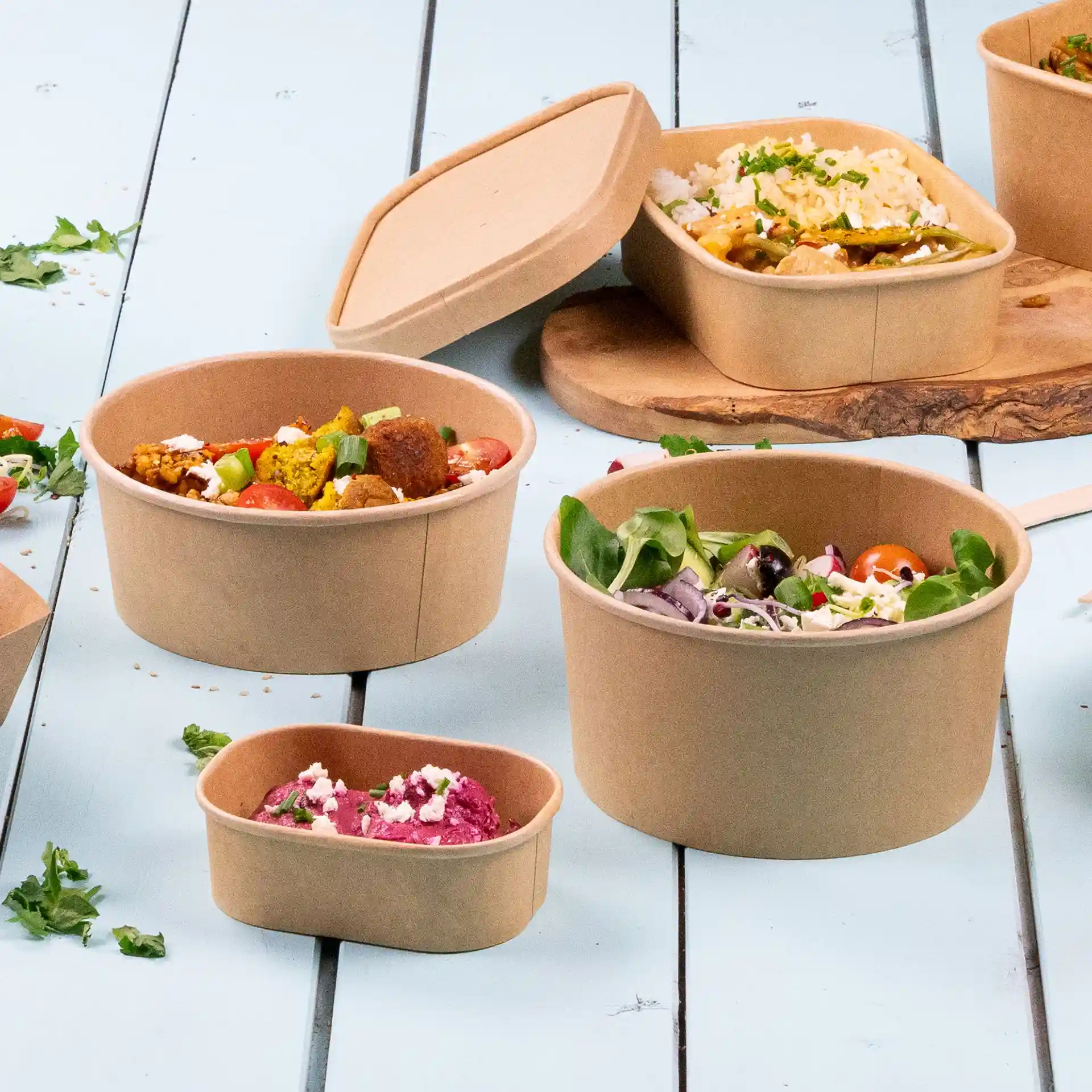 Runde braune Papierschalen mit umweltfreundlicher Beschichtung, verschiedene Größen, auf einer hellblauen Oberfläche präsentiert.