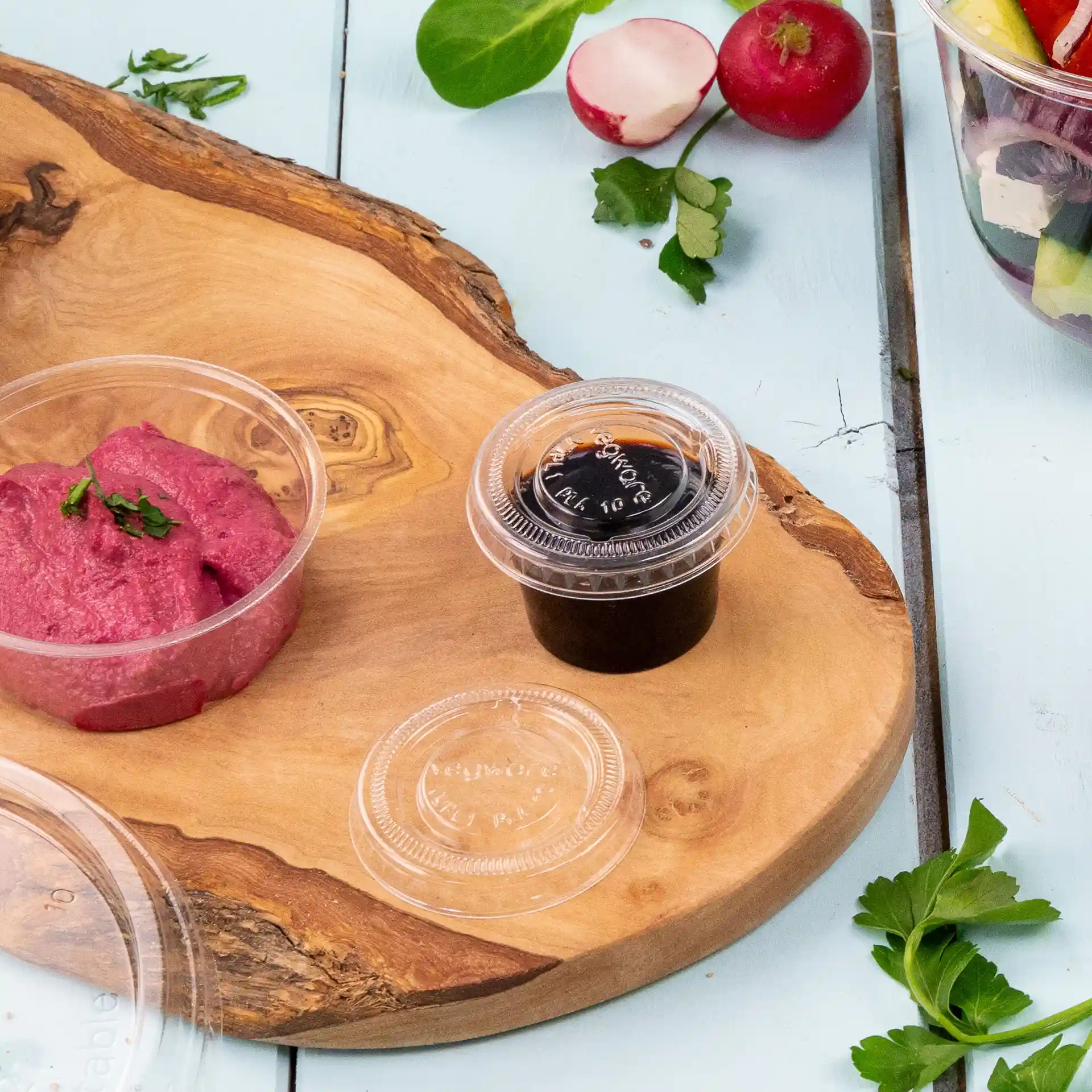 Bild eines Holzservierbretts mit einem rosa Dip in einem klaren Behälter und einer dunklen Sauce in einem anderen klaren Behälter.