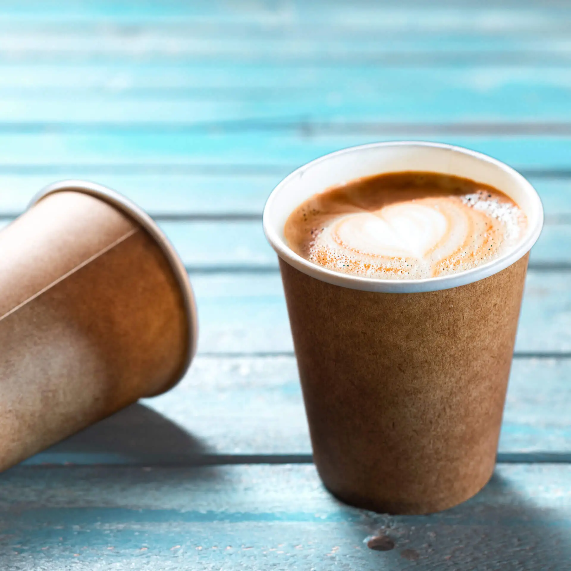 Brauner Becher mit weißer Innenauskleidung, gefüllt mit Kaffee, auf einer blauen Holzoberfläche.
