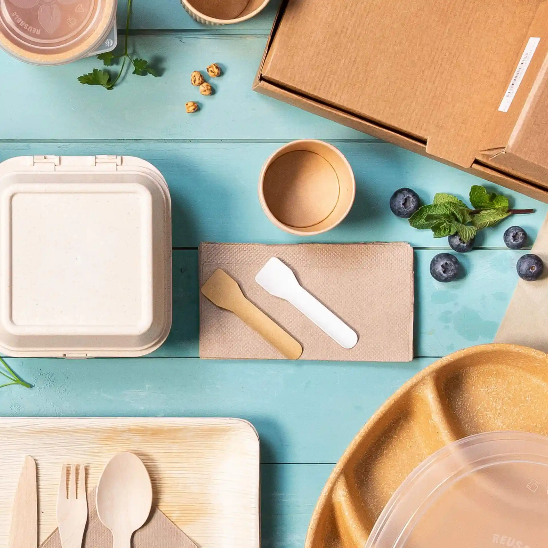 Image of various disposable food containers, utensils, and a cardboard box on a blue surface.