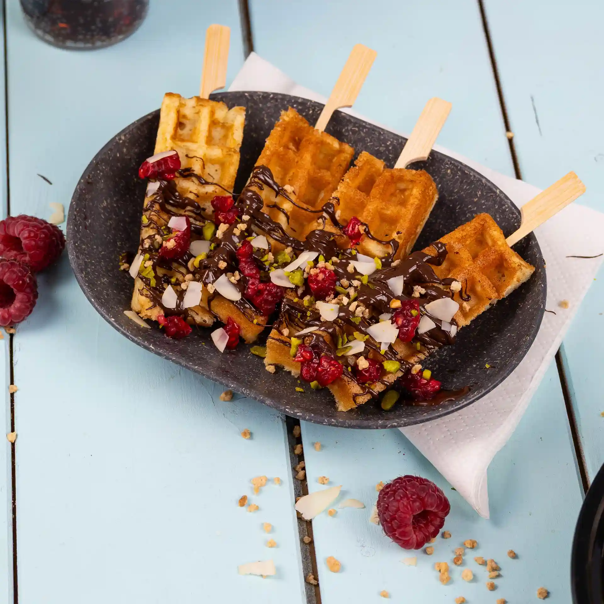 Plate with three waffles topped with chocolate, raspberries, and nuts, served on a grey oval dish.