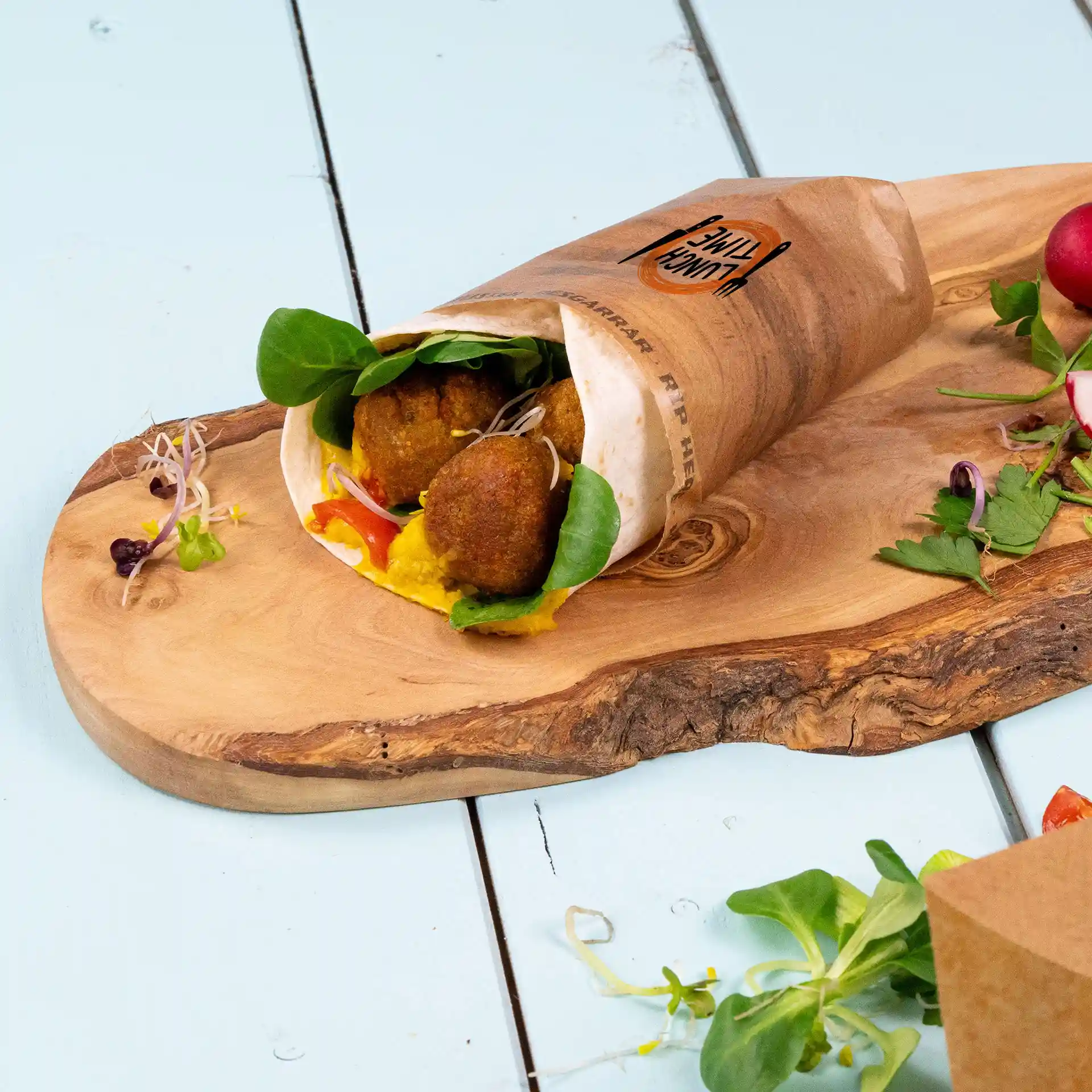 Wrap-Tasche mit Falafel, Gemüse und Sauce, auf einem Holzbrett mit zusätzlichem Gemüse daneben.