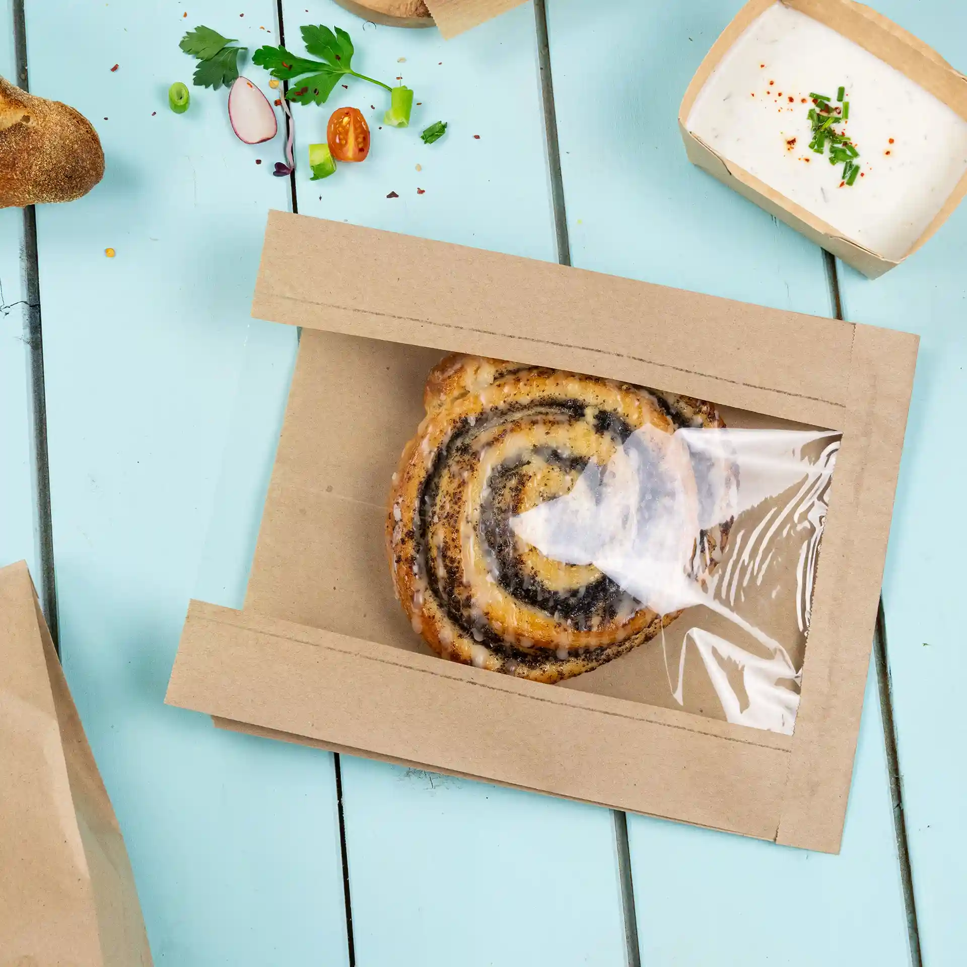 Brown flat paper bread bag with a transparent window, containing a spiral pastry, on a light blue surface.