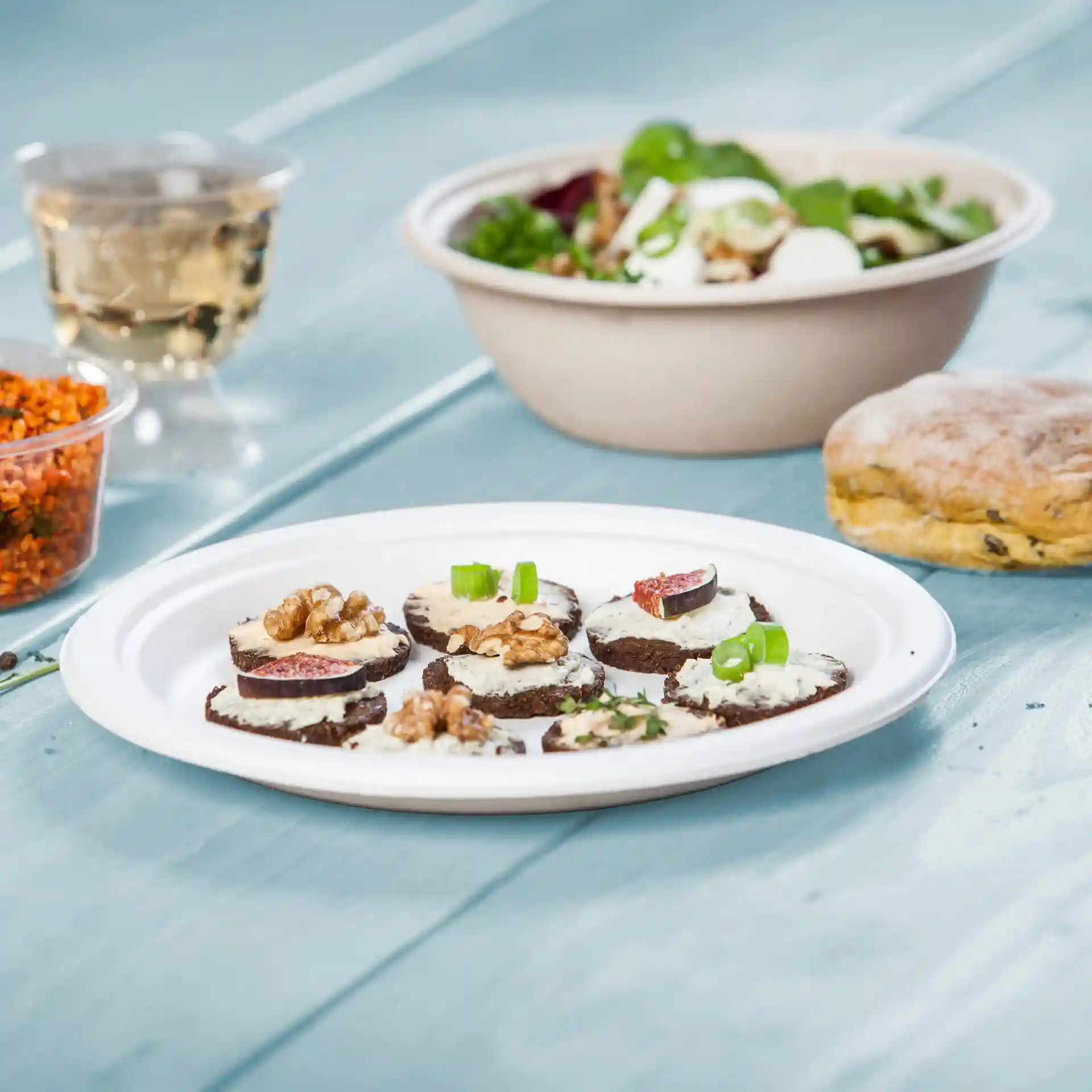 Teller mit mehreren runden Scheiben dunklem Brot, belegt mit Sahne, Walnüssen und Feigen, dazu ein Salat und ein Keks.