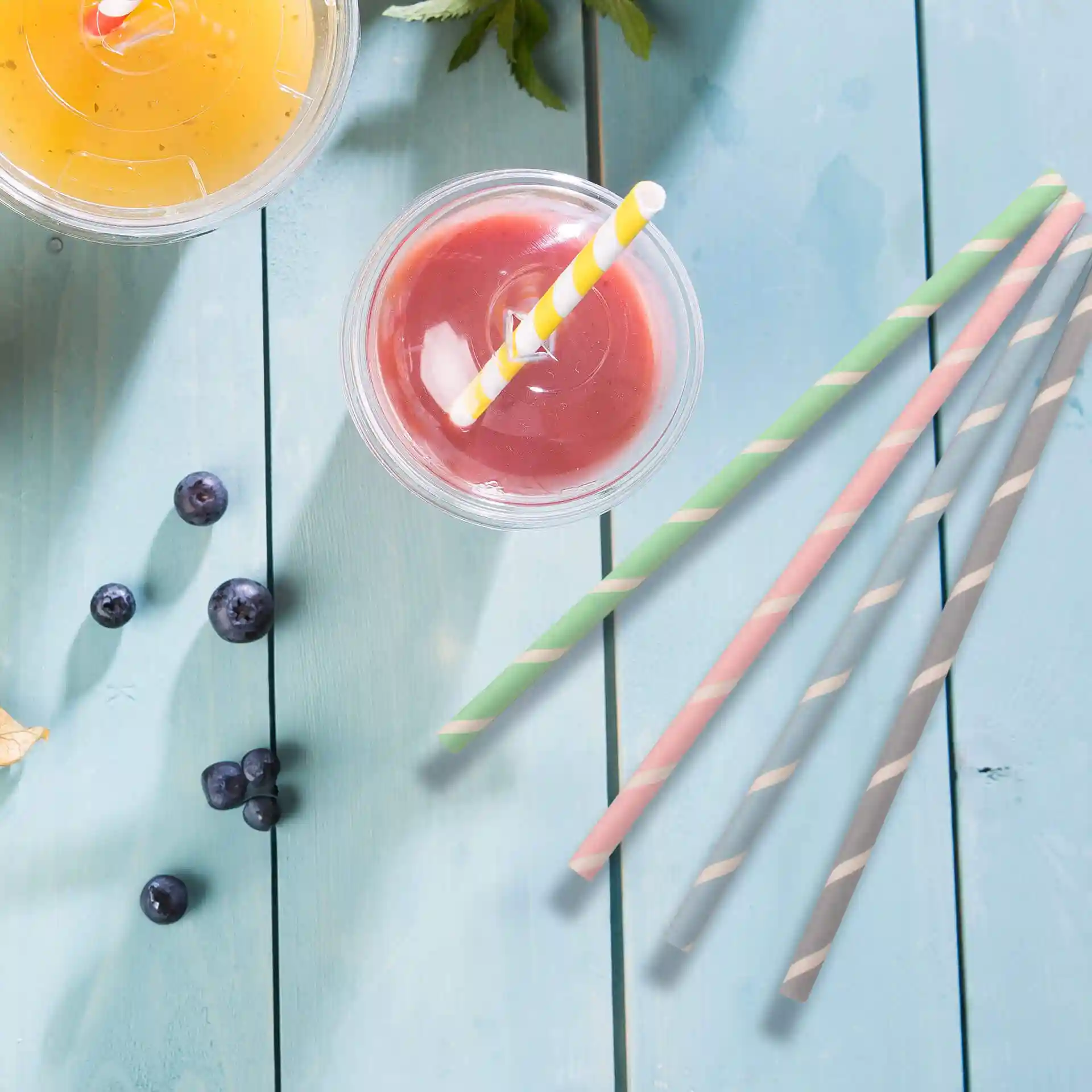 Image of two drinks in clear cups with straws, surrounded by blueberries and four pastel striped paper straws.