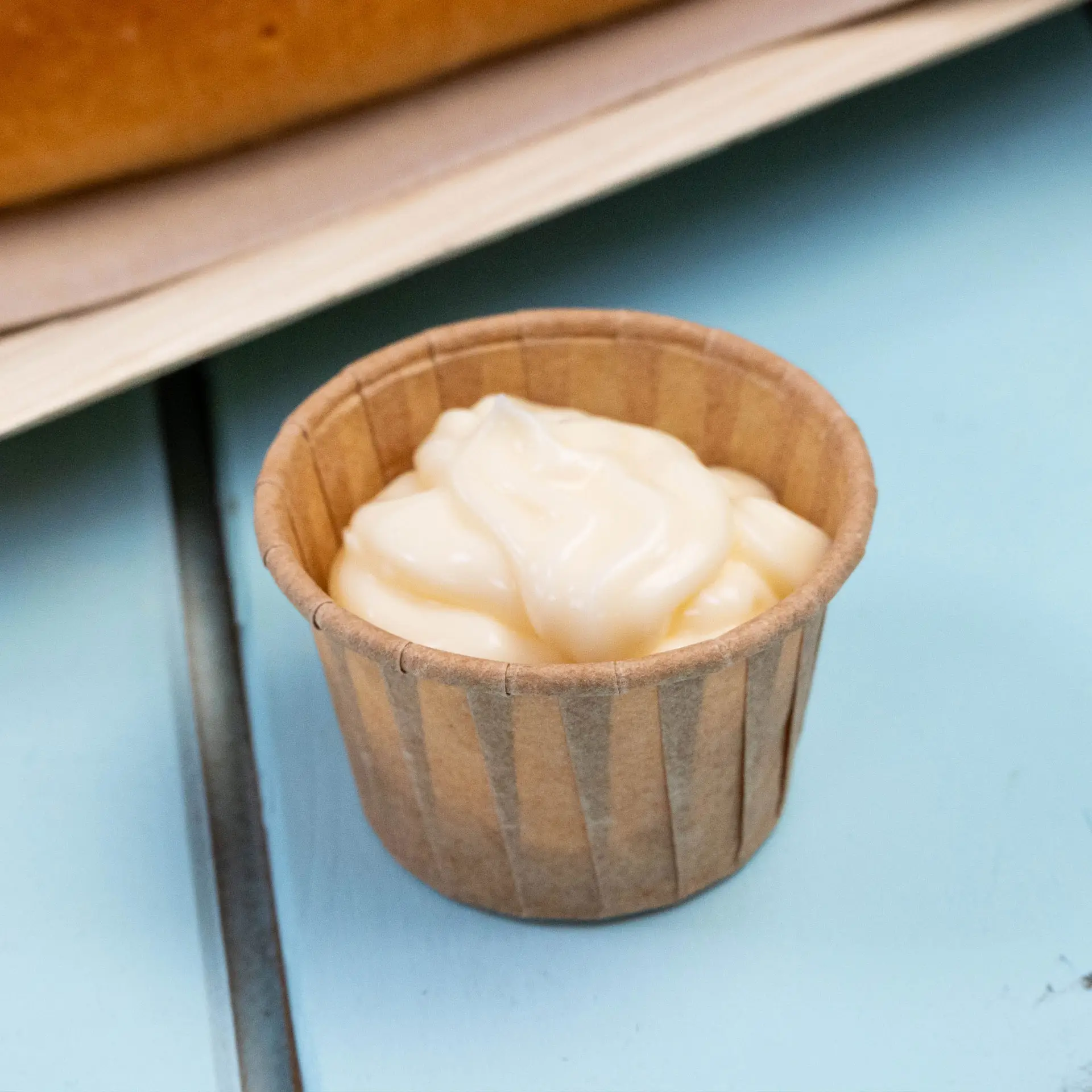 Small brown paper cup containing a creamy dip, placed on a light blue surface.
