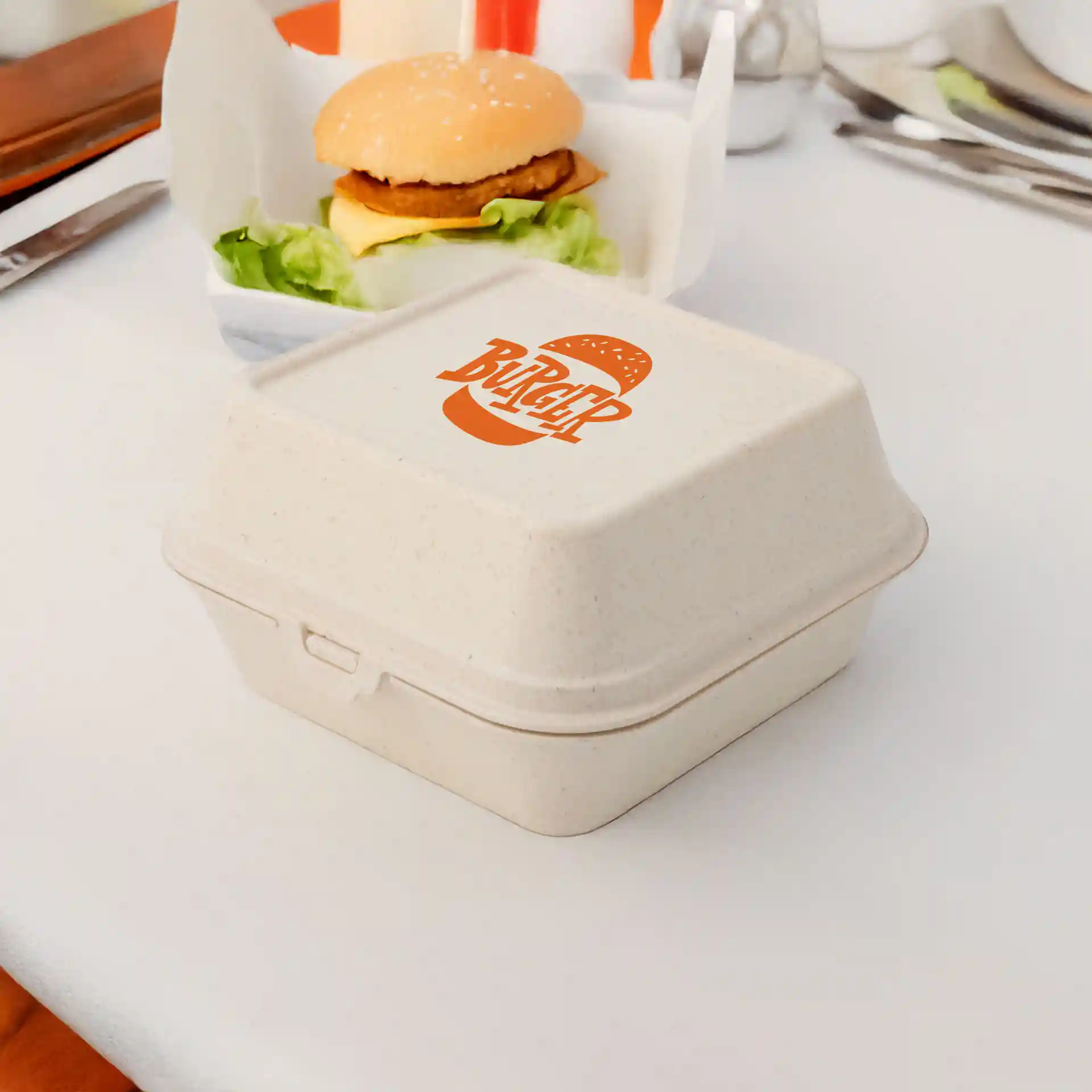 Cream white rectangular burger box with a printed logo, placed on a table next to a burger and lettuce.