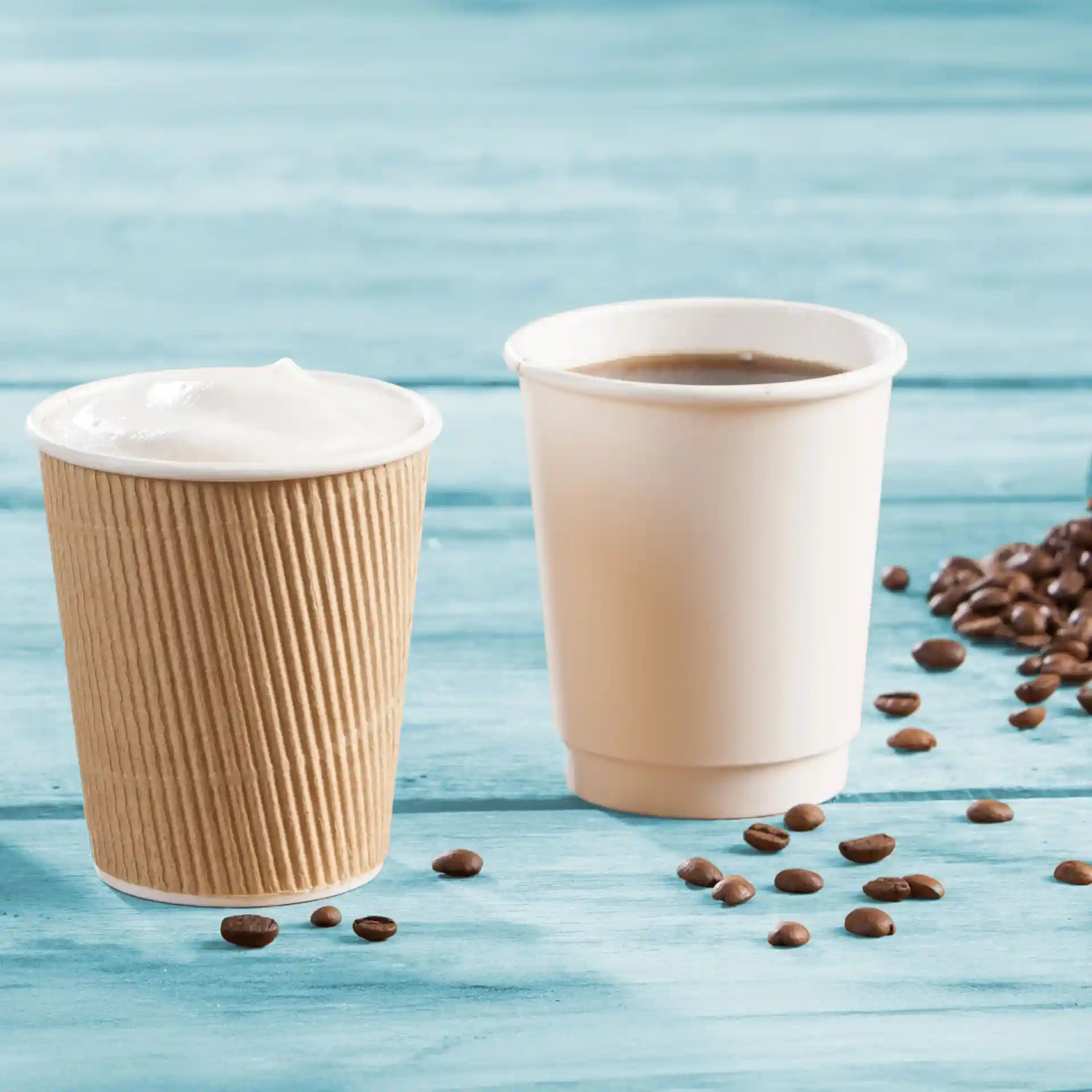 Doppelwandige Pappbecher in Braun und Weiß, mit Kaffeebohnen auf einer blauen Holzoberfläche verstreut.