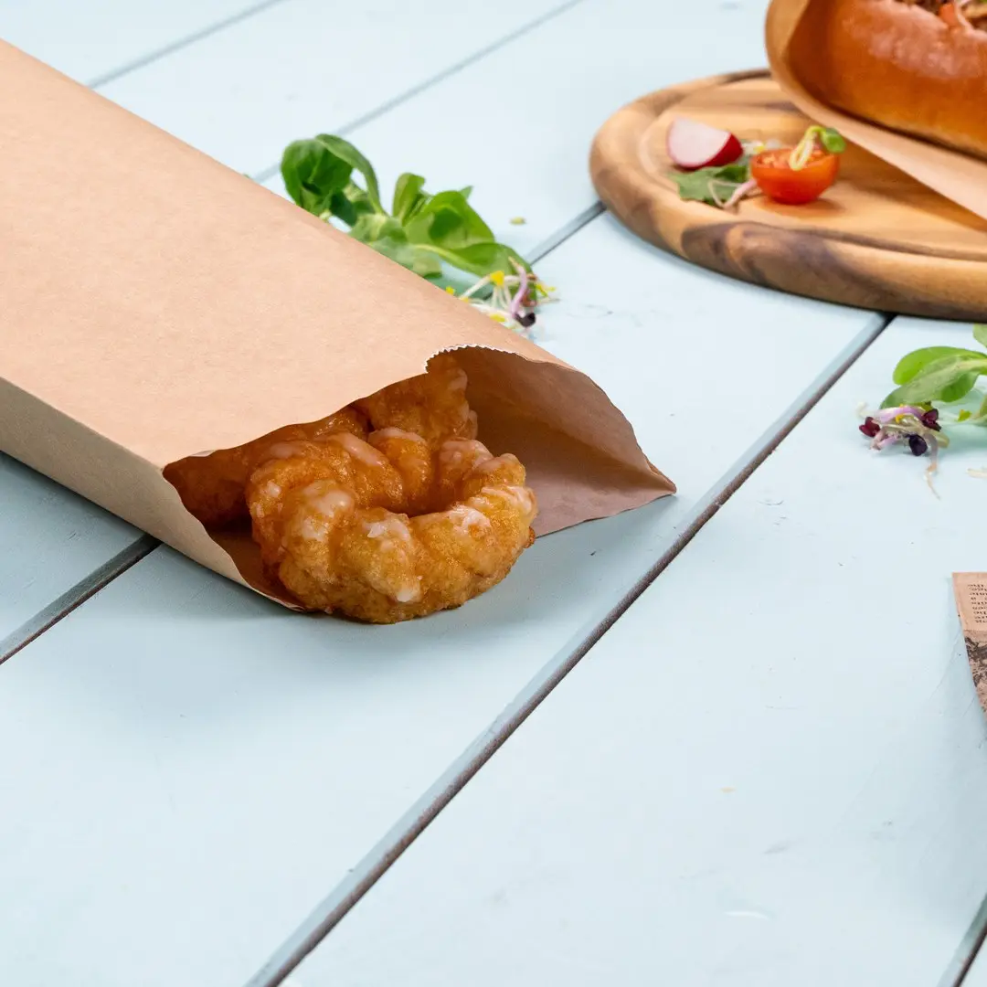 Brown paper bag partially open with a pastry inside, placed on a light blue wooden surface.