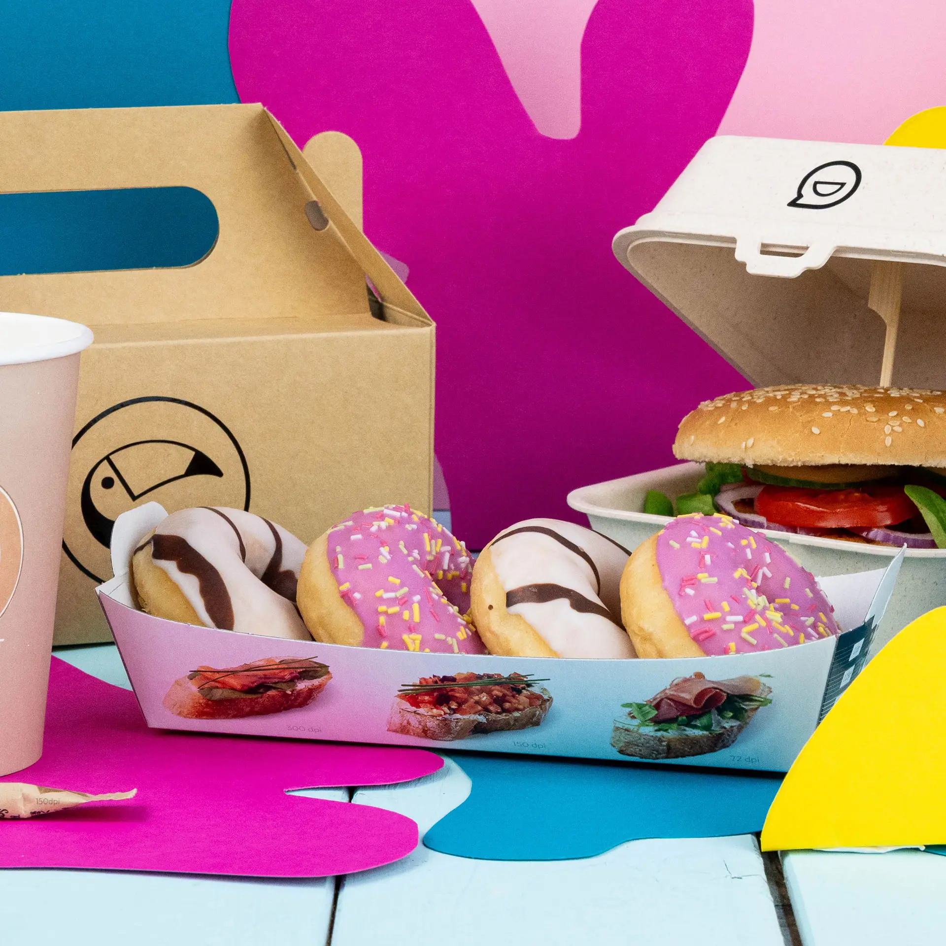 Rectangular printed cardboard snack tray with four donuts, a burger, and a coffee cup against a colorful background.