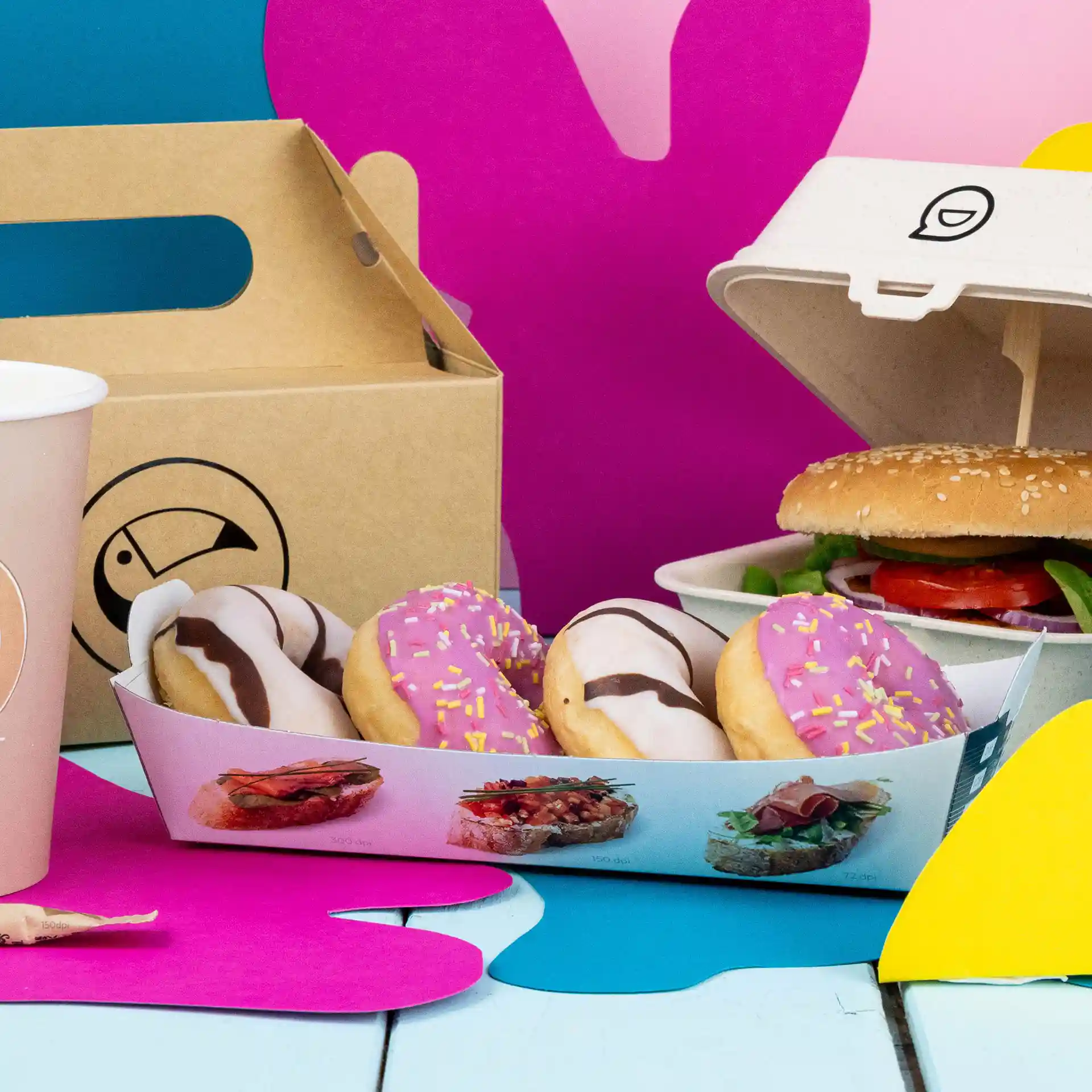 Rechteckige weiße Snackplatte mit vier Donuts, einem Burger in einem Behälter und einem pinken Becher auf einem bunten Hintergrund.