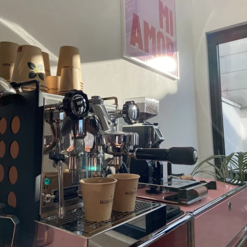 Kaffeemaschine mit zwei braunen Bechern auf einer Theke, in einem Café mit Wandkunst "MI AMOR."