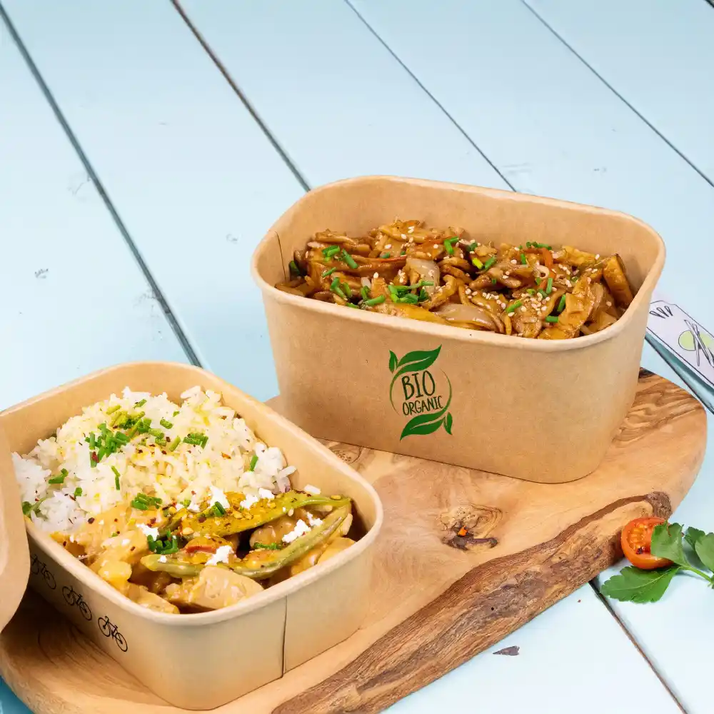Brown biodegradable food containers filled with rice and vegetables on a wooden board.
