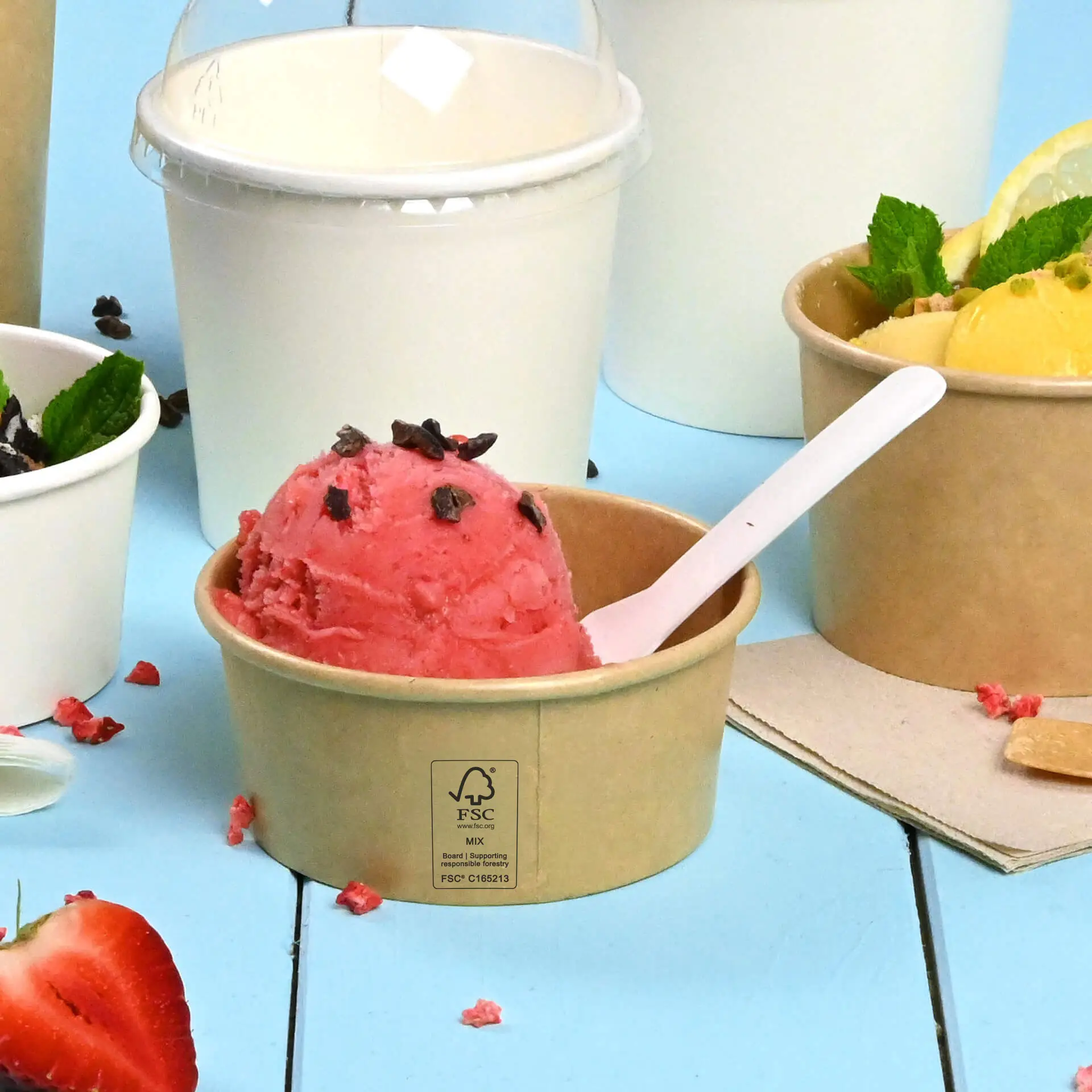 A brown, PE-coated ice cream cup with pink ice cream and chocolate sprinkles; other ice cream containers are partially visible.