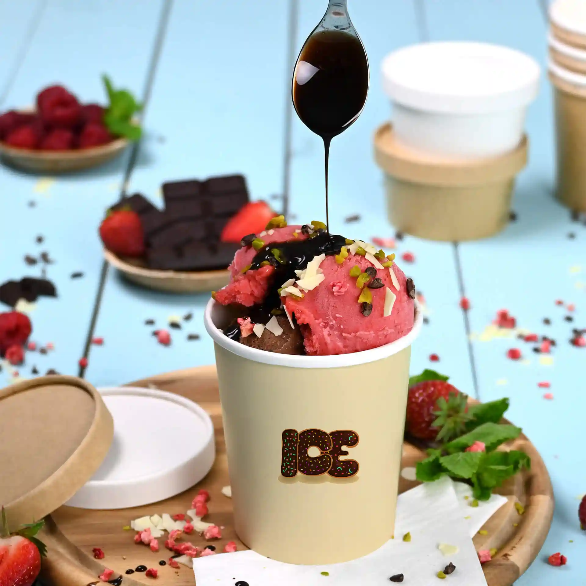 Runder weißer Becher mit rosa und braunen Eiskugeln, garniert mit Schokoladensauce und Nüssen, auf einem Holztablett.