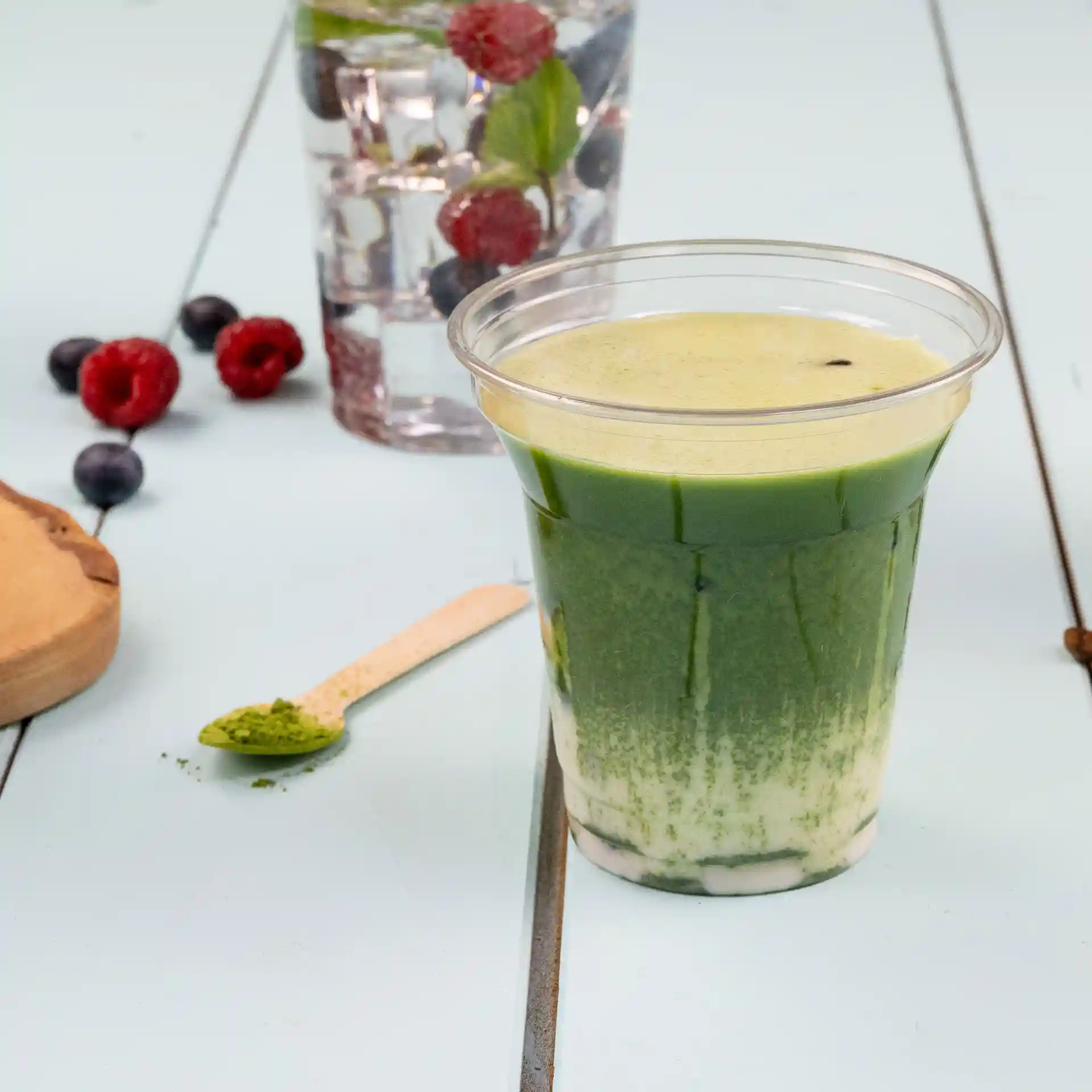Klarer rPET-Becher gefüllt mit grünem Getränk, mit einem Holzlöffel und Beeren im Hintergrund.