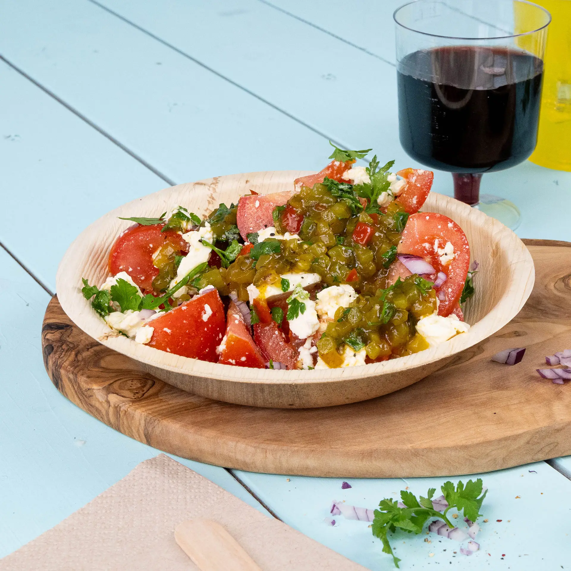 Ein tiefes, rundes Teller aus Palmblättern gefüllt mit einem Salat aus Tomaten, Kräutern und Jalapeño, auf einem Holzbrett mit einem Getränk.