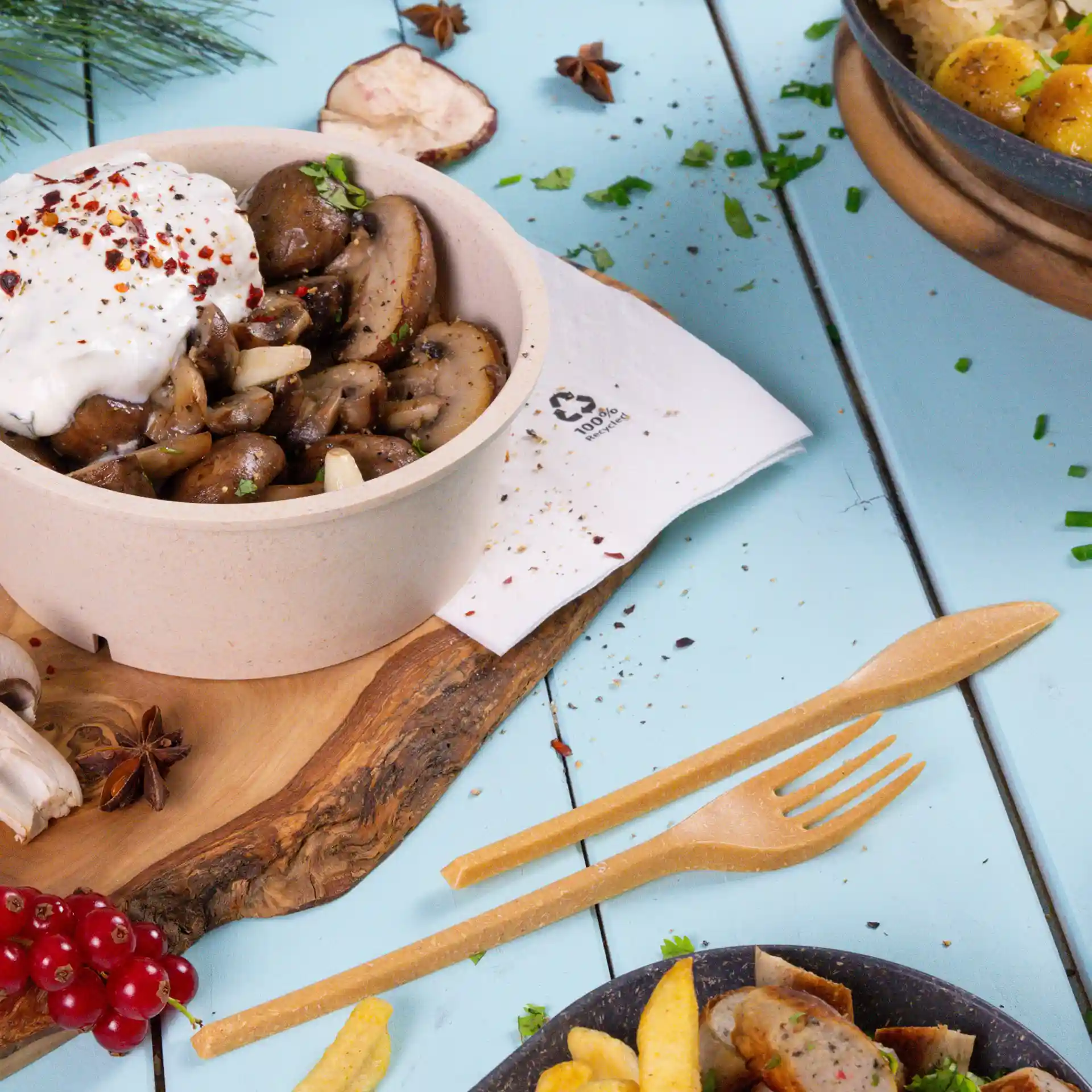 Schüssel mit sautierten Pilzen, garniert mit Joghurt und Gewürzen, begleitet von einer Holzgabel und -messer auf einem blauen Tisch.