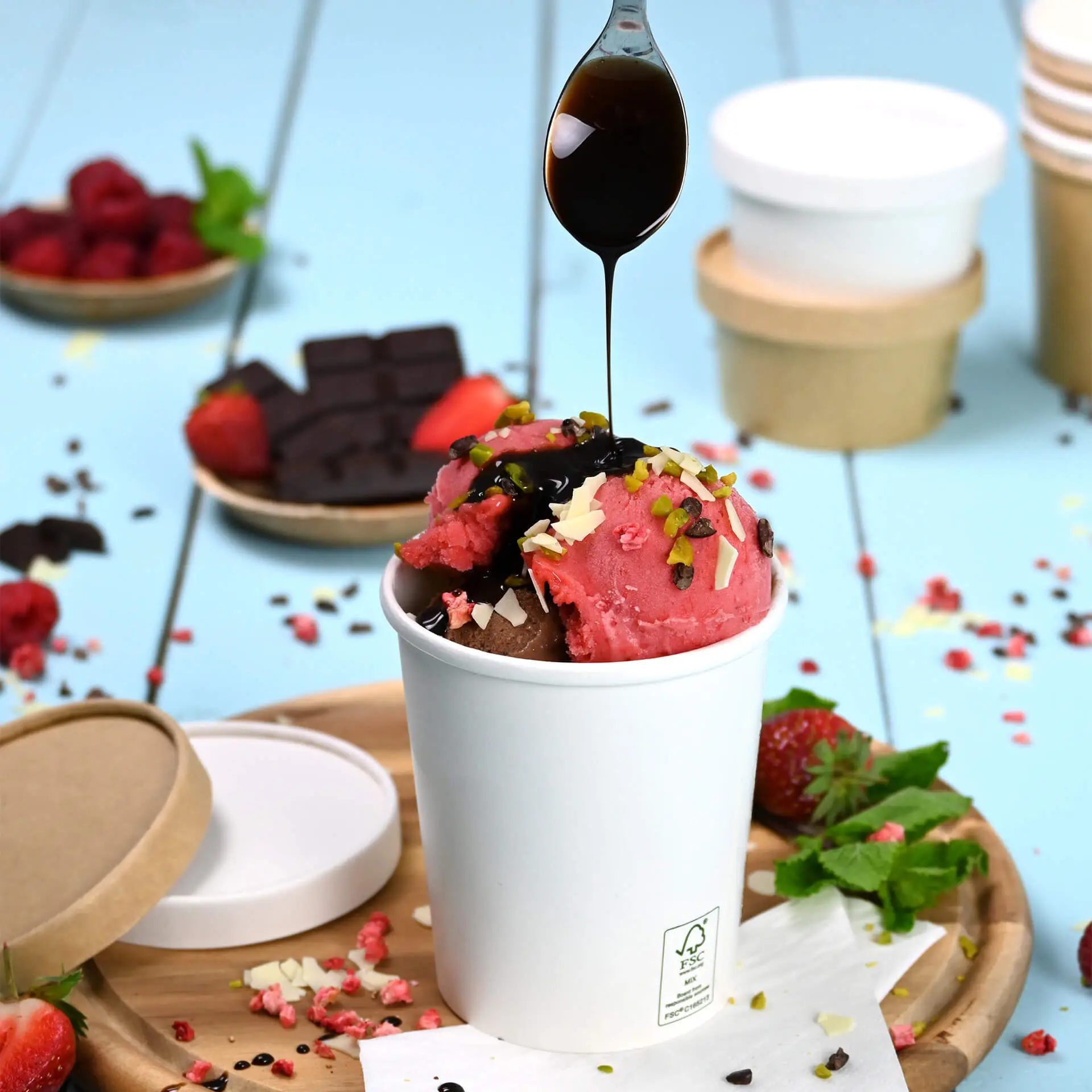 A white paper ice cream cup filled with chocolate and strawberry ice cream, topped with various toppings and chocolate sauce.