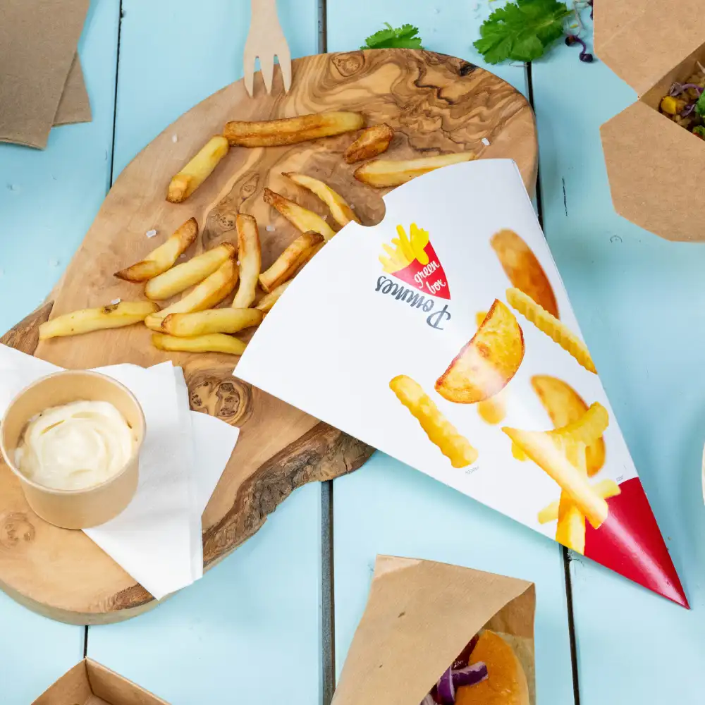 Papiercone mit Pommes Frites und Kartoffelspalten; Beilage von Dip-Sauce und verstreuten Pommes auf einem Holzbrett.