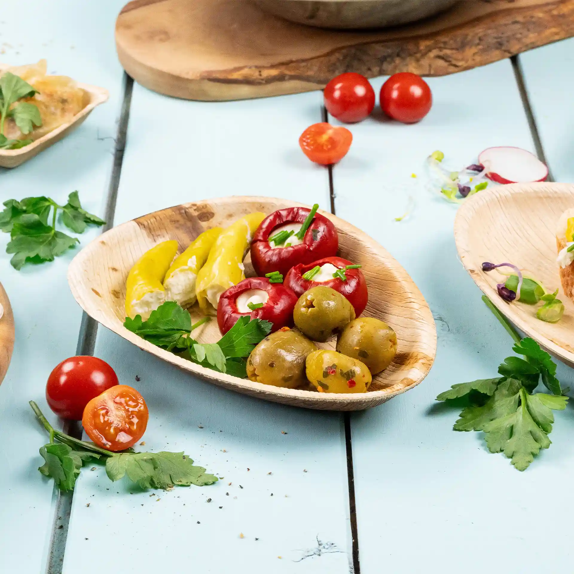 Ovaler Palmblatt-Teller mit verschiedenen Oliven, gefüllten Paprika und Kirschtomaten, garniert mit Petersilie.