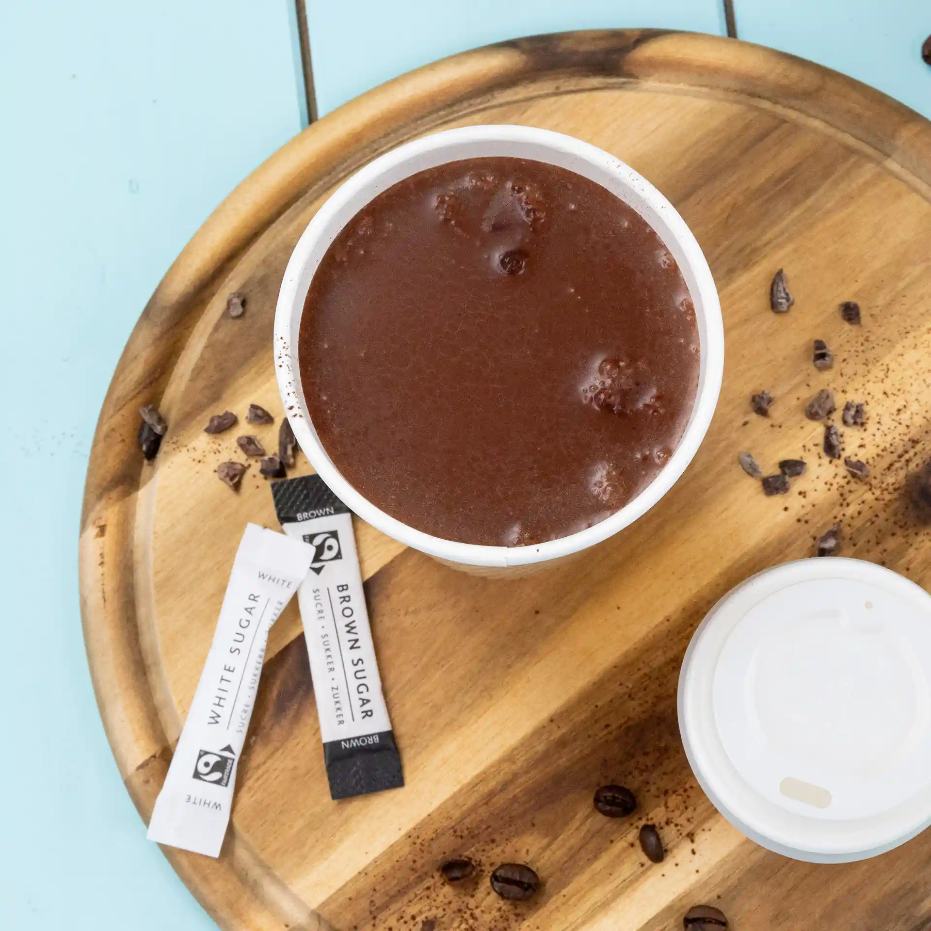 Becher mit heißer Schokolade auf einem Holztablett, umgeben von Zuckersticks und verstreuten Kaffeebohnen.