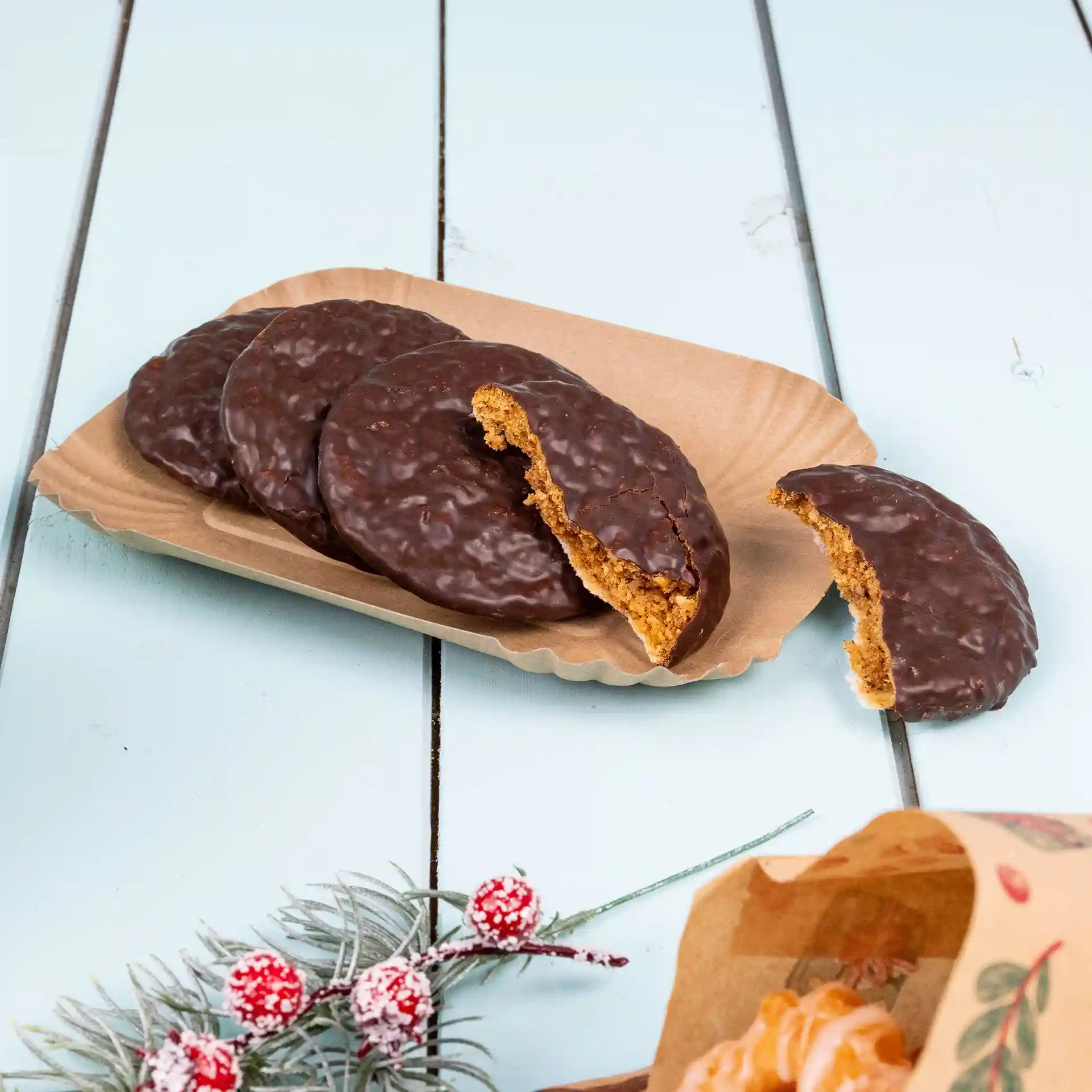 Brown cardboard food tray with several chocolate-covered cookies, one partially bitten, on a light blue surface.