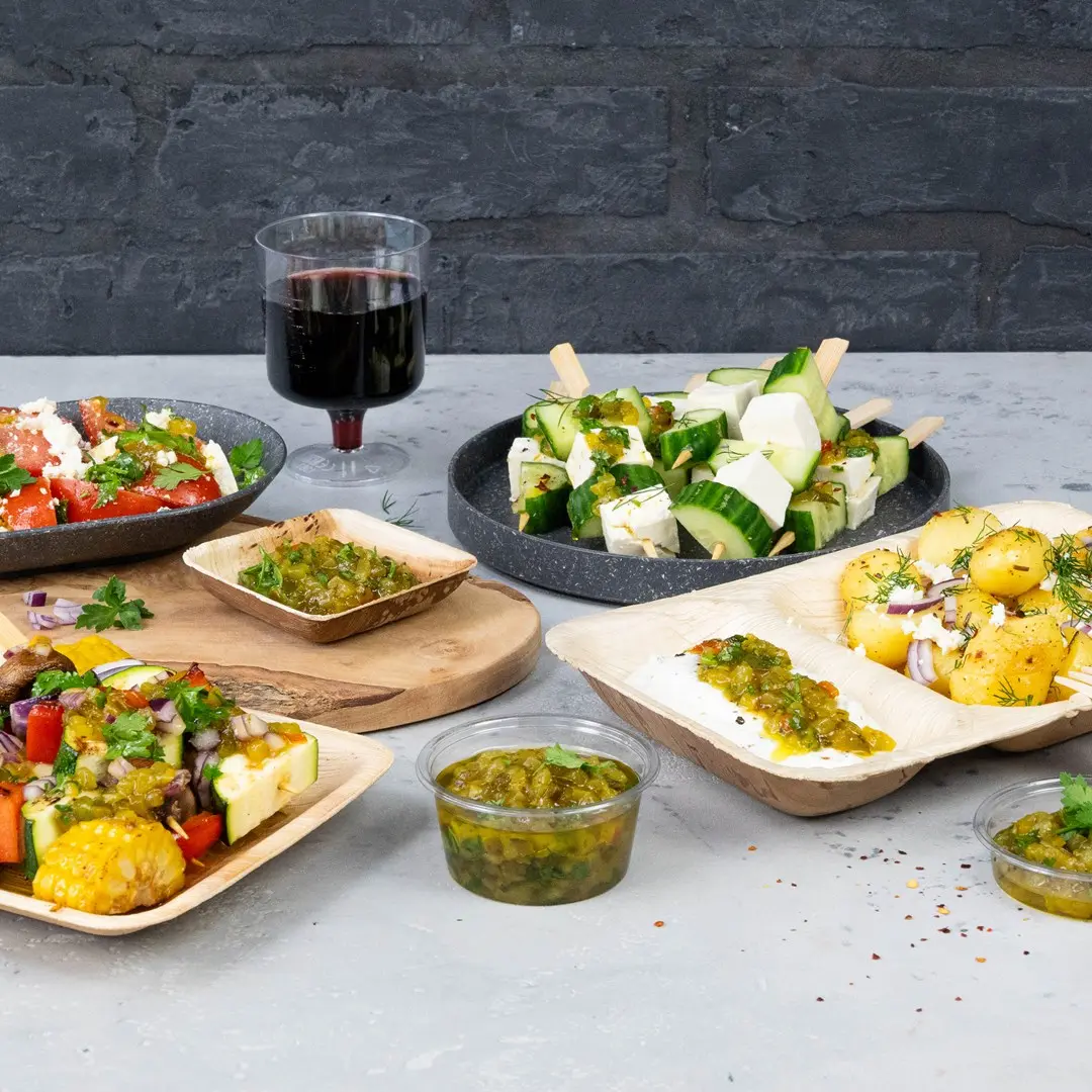 Eine Auswahl an Fingerfood, darunter Salate, Gurken- und Käse-Spieße sowie Saucen, mit einem Glas Rotwein im Hintergrund.