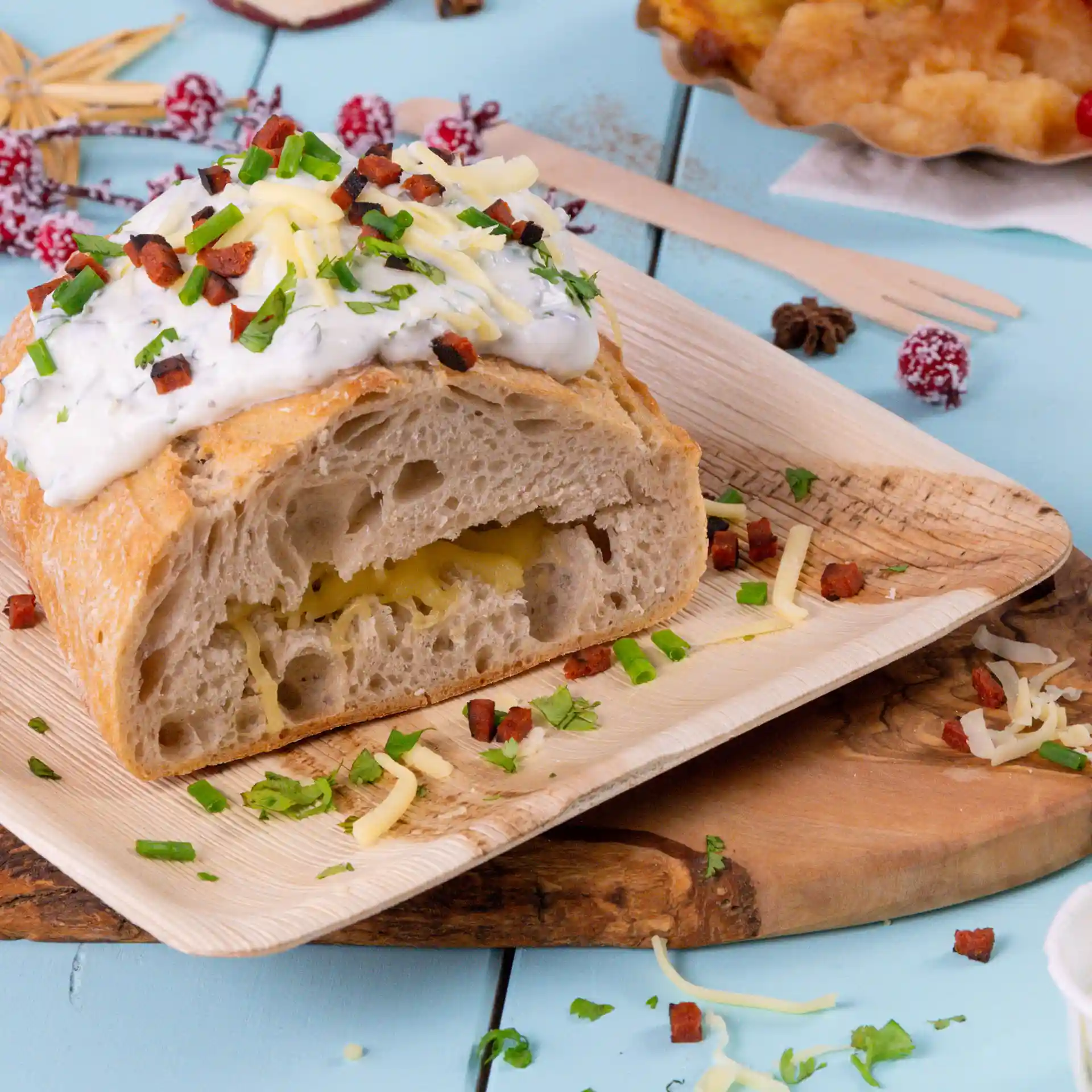 Square palm leaf plate with a cut loaf of bread topped with sauce, cheese, and herbs, on a wooden surface.