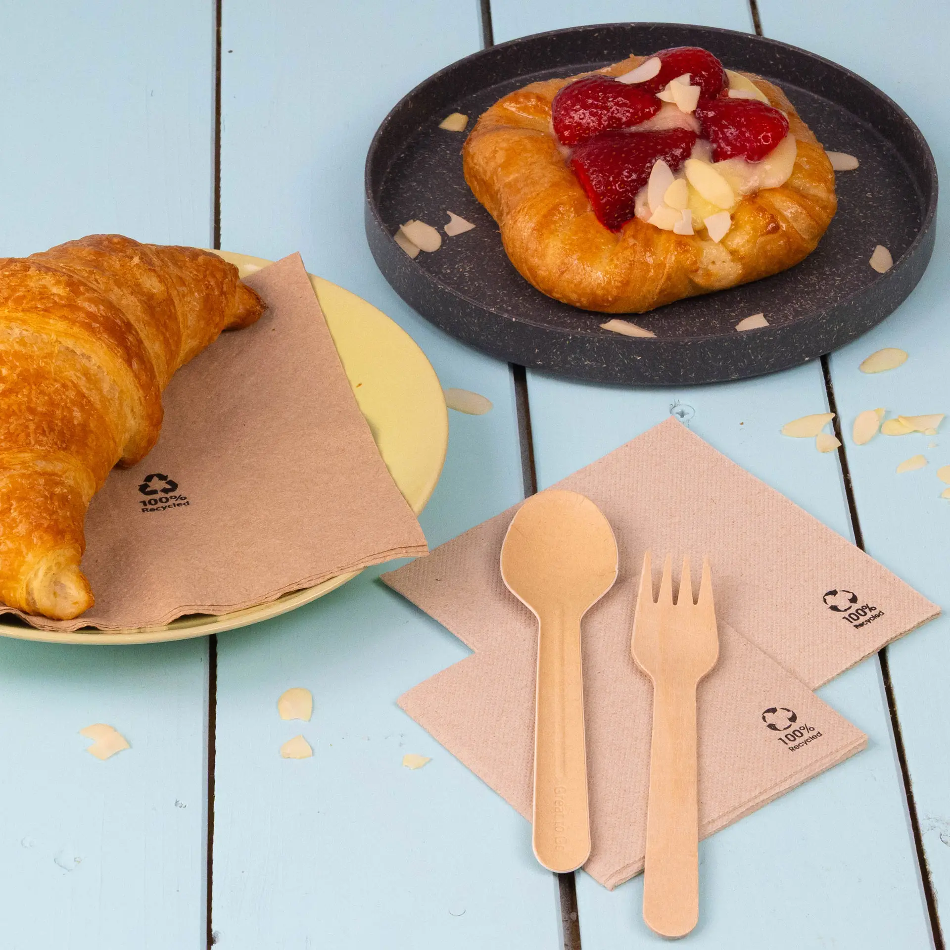 One white coffee cup with a biscuit on a white plate, surrounded by a bowl of raspberries and cocktail napkins made of recycled paper.