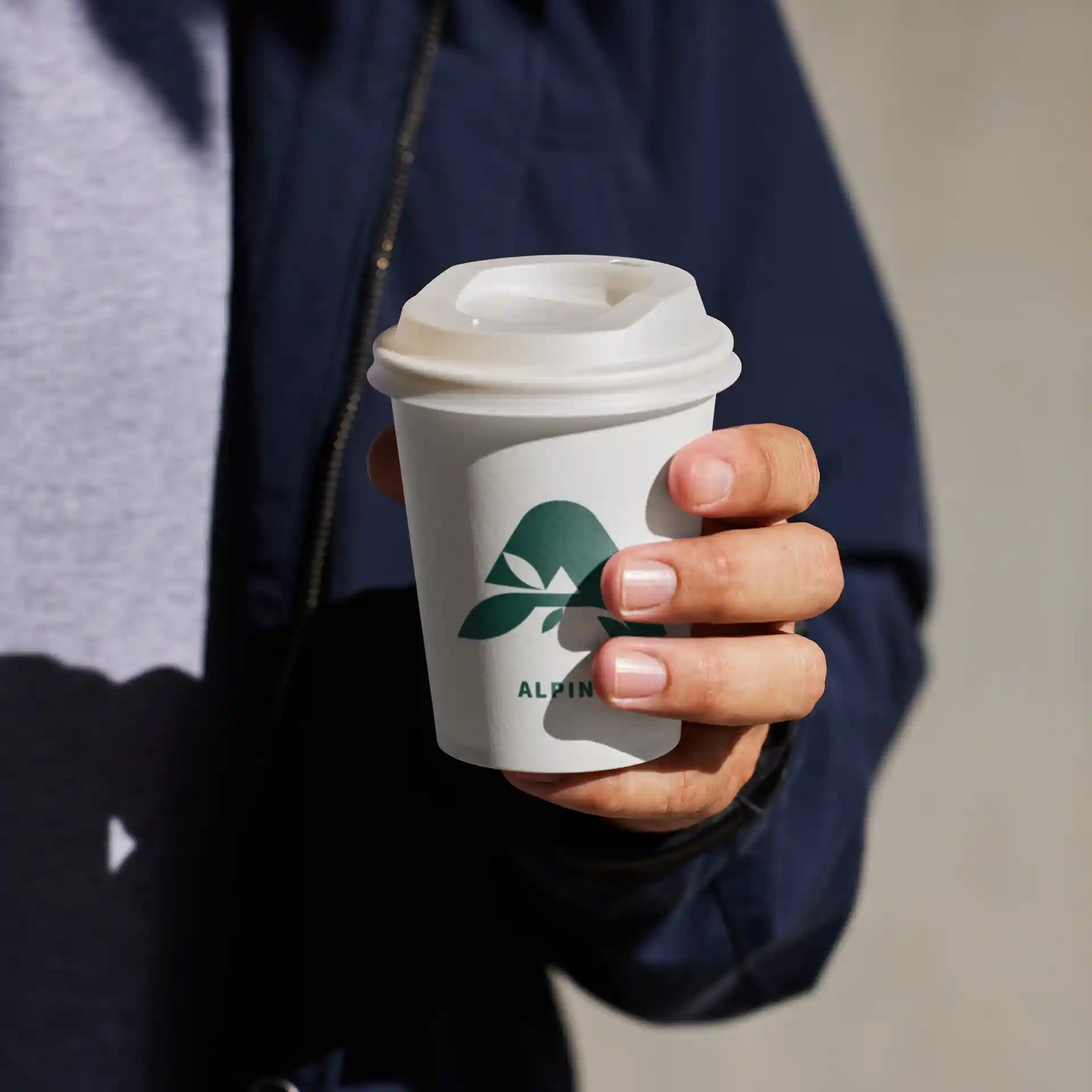 White paper cup with a green logo, held in a hand, featuring a lid and a round shape.