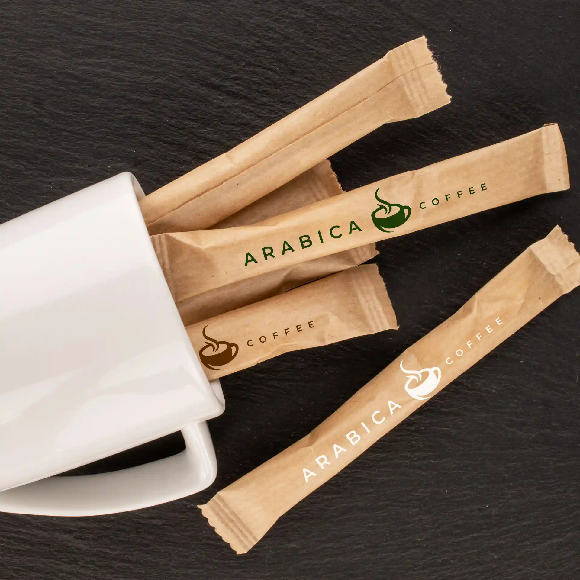 Braune Zuckersticks mit Logo neben einem weißen Becher auf einer dunklen Oberfläche.