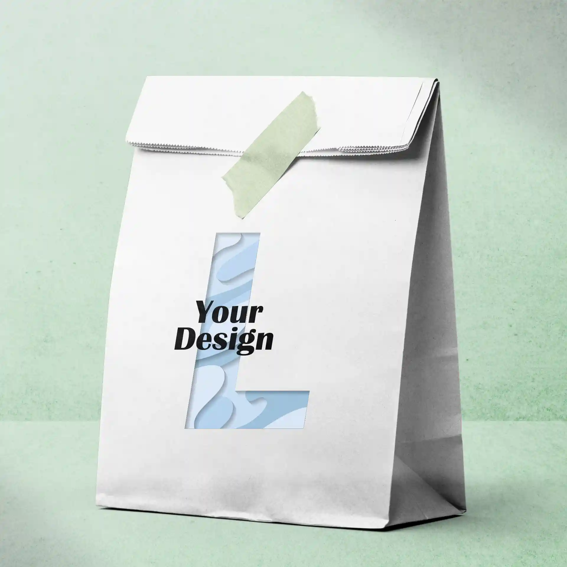 Weißer Papiertüte mit ausgeschnittenem Buchstaben 'L' und dem Text 'Dein Design', mit grünem Klebeband gesichert.