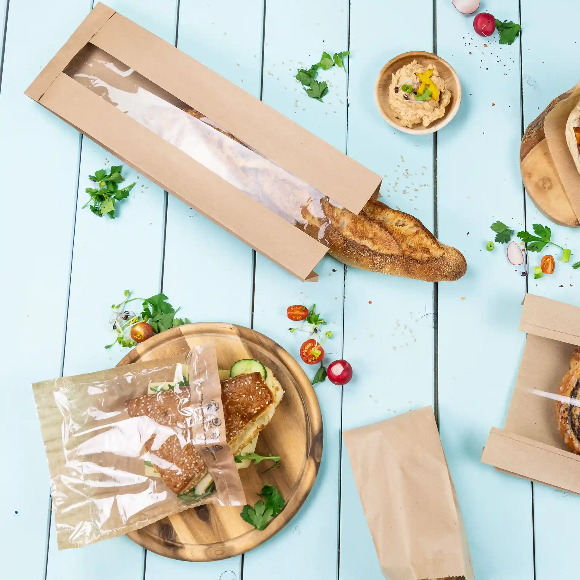 Brown flat paper bread bag with a window, placed on a blue wooden surface with a sandwich and other food items.