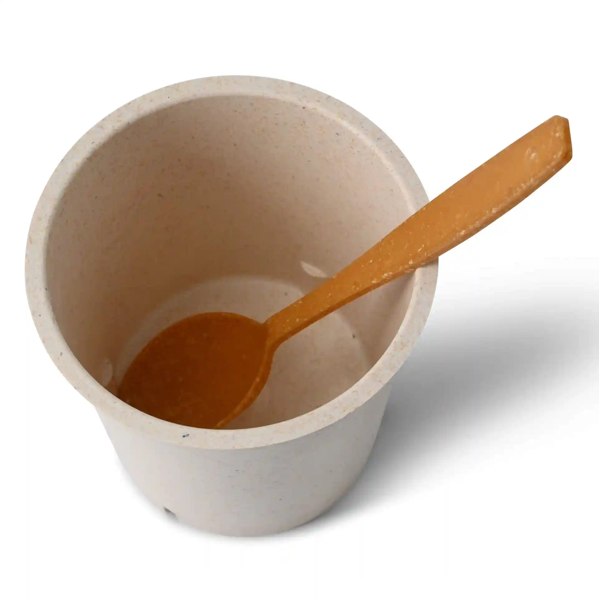 Runder cremeweißer wiederverwendbarer Becher mit einem passenden orangefarbenen Löffel darin, von oben gezeigt.