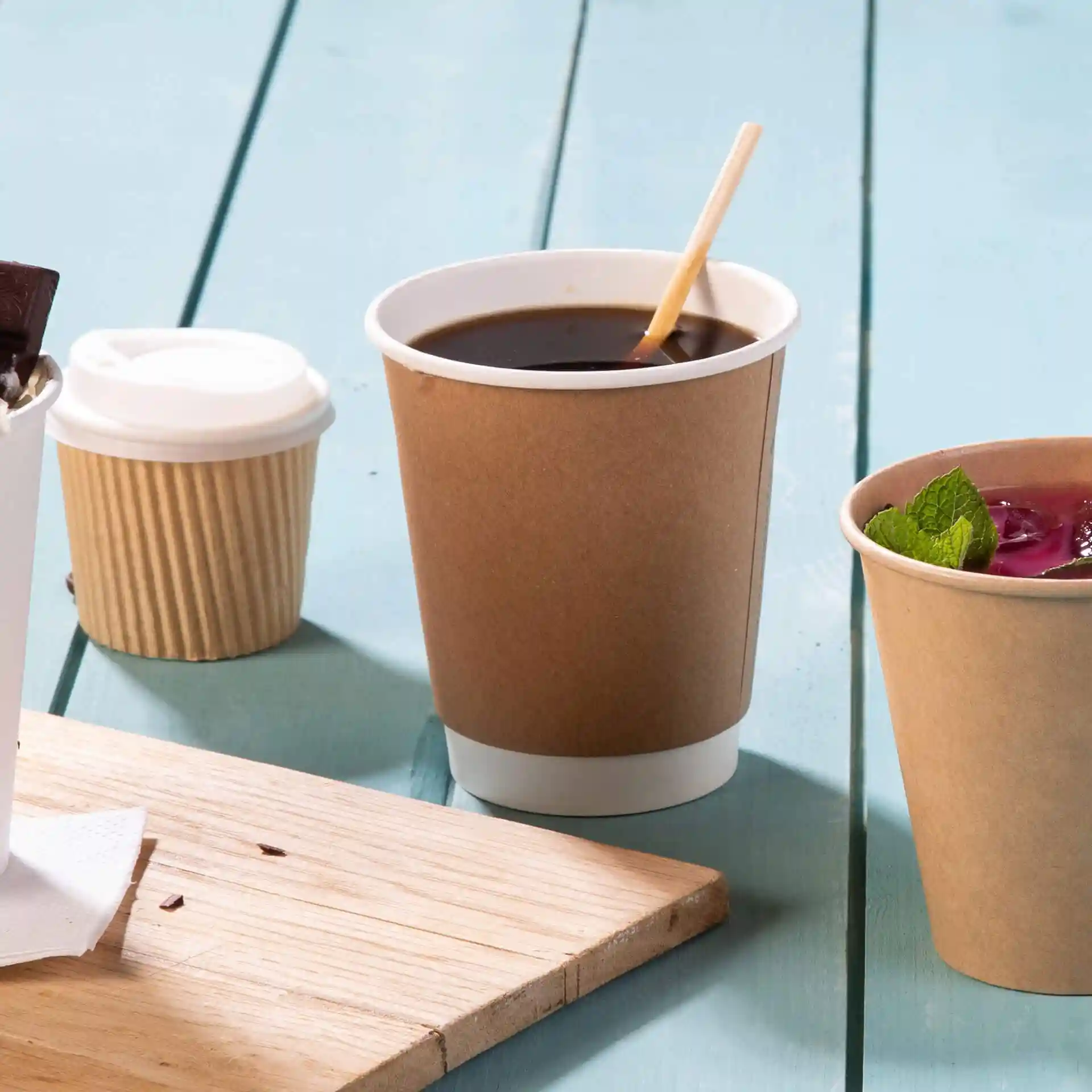 Brown double-walled cardboard coffee cup with a white inner lining, surrounded by other cups on a wooden surface.