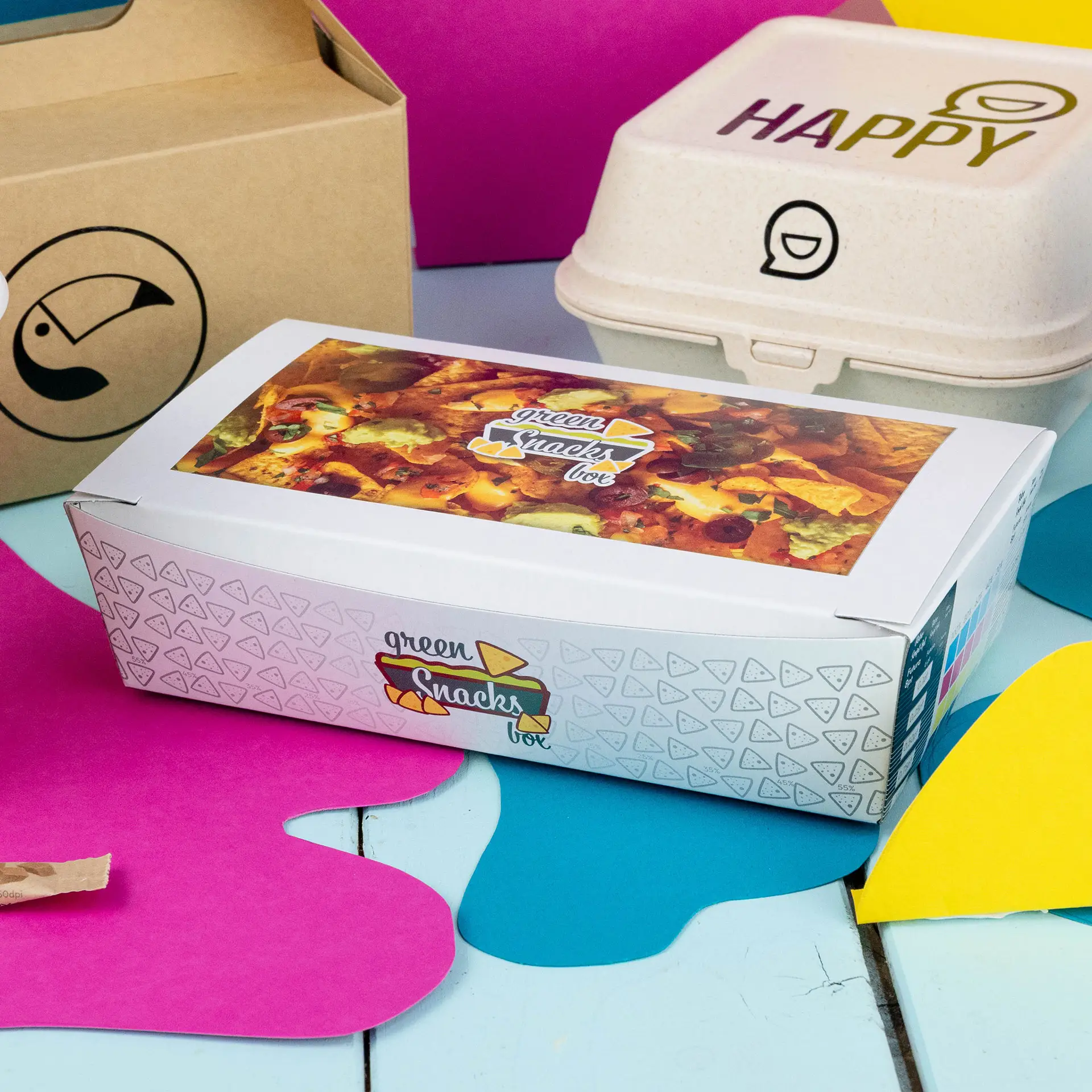 White snack box with a colorful printed design, labeled for snacks, on a vibrant background with similar packaging nearby.
