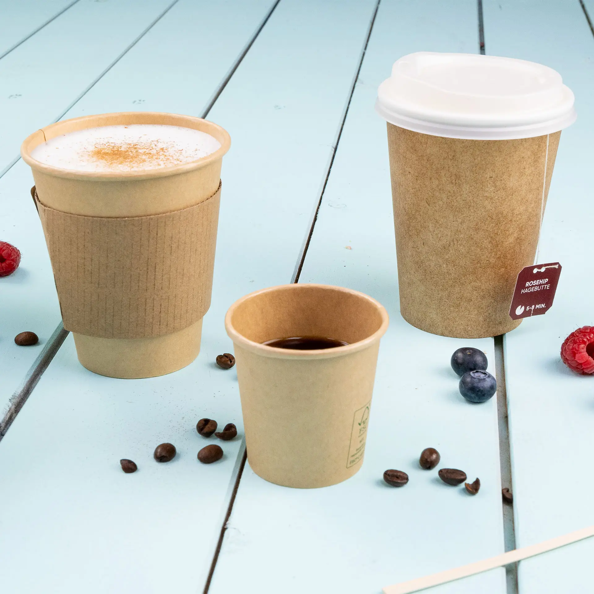 Bild von drei braunen Bechern in verschiedenen Größen auf einer blauen Holzoberfläche, mit Kaffeebohnen und Beeren verstreut.
