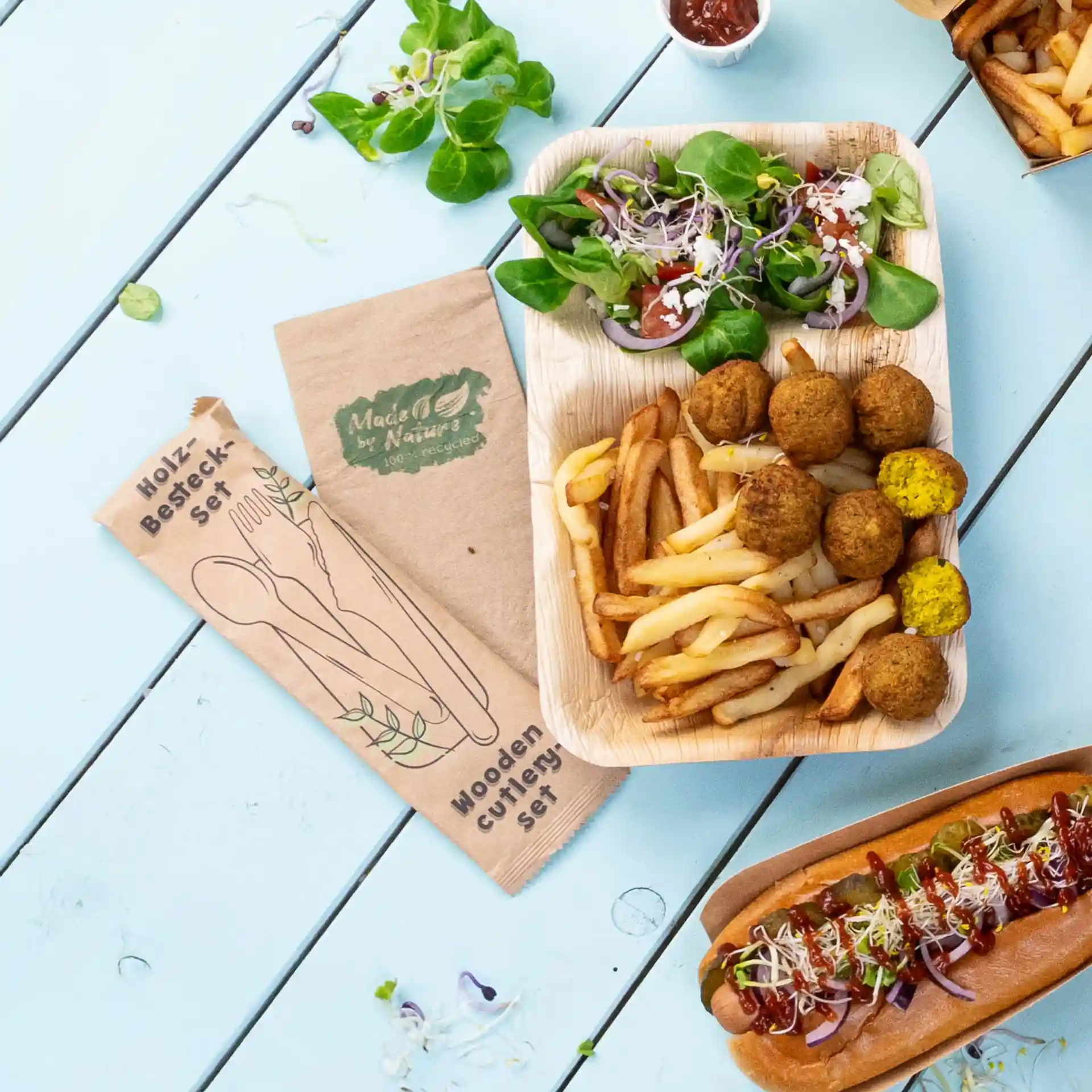 Image of a wooden cutlery set with a knife, fork, and spoon, alongside a plate of fries, falafel, and salad.