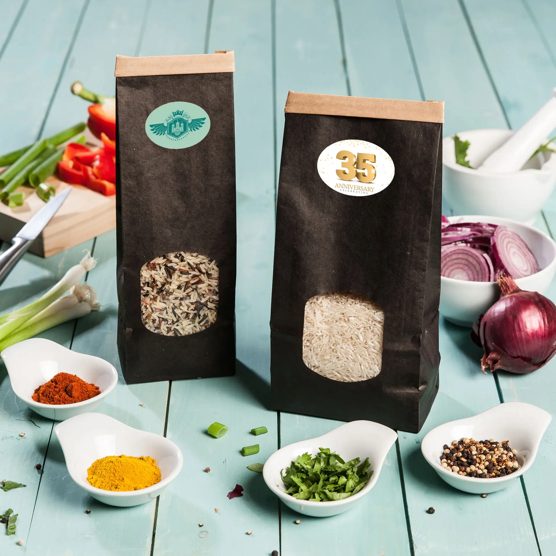 Two black paper bags of rice, one with a window revealing long grain rice and the other with mixed rice, with spices and vegetables around.